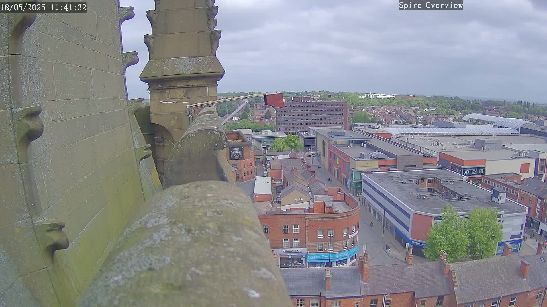 A high-angle view from a stone structure on an overcast day shows a town square with buildings and a shopping center below.