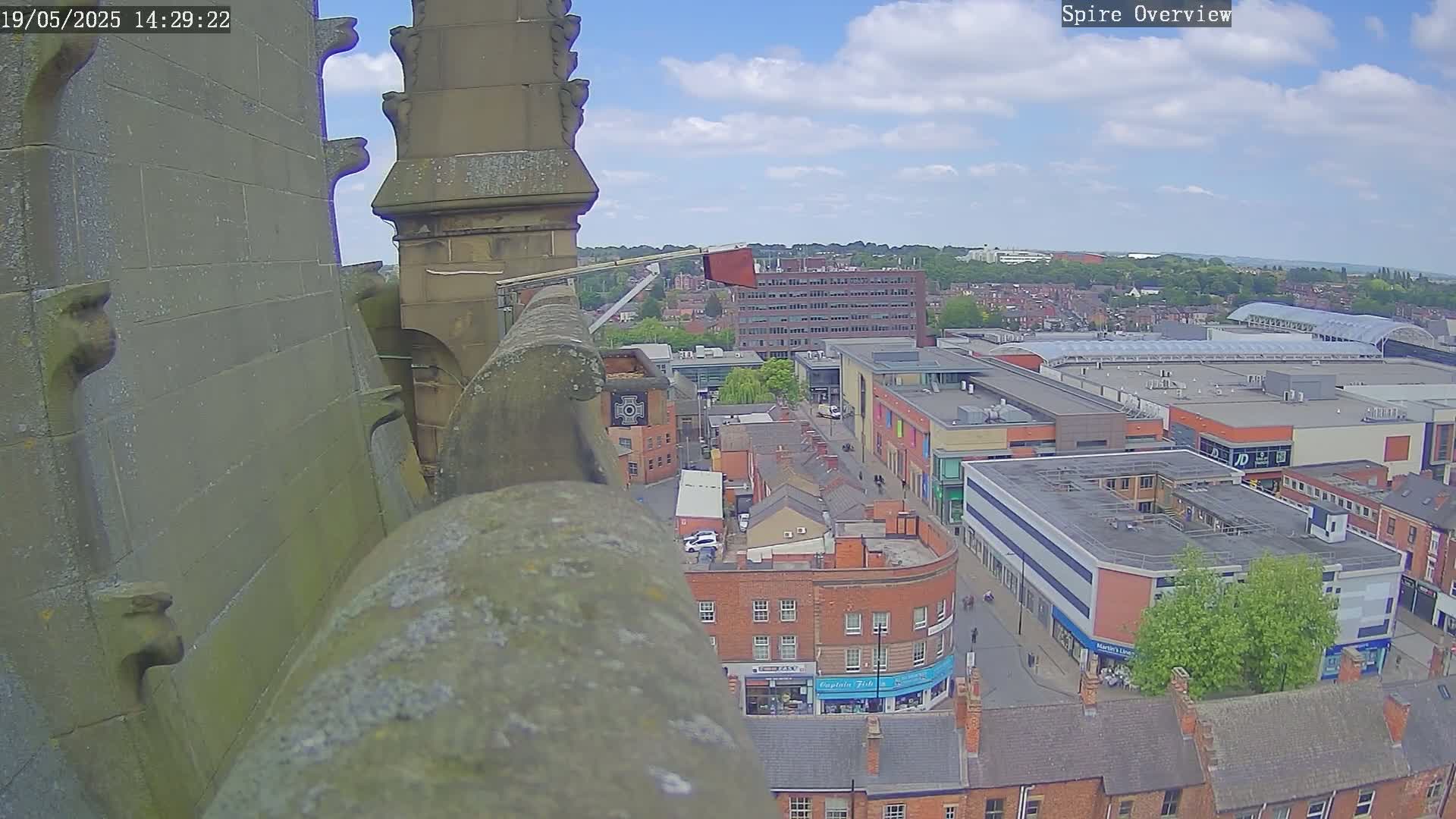 A high-angle view from a stone structure shows a town square with buildings under a partly cloudy sky.