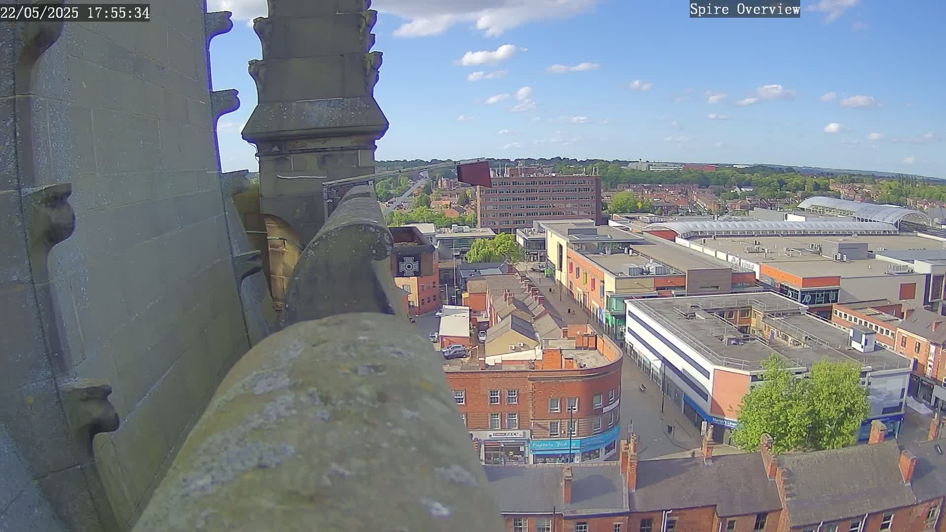 A high-angle view on a sunny day shows a city center with a shopping mall and numerous brick buildings from a stone structure's vantage point.