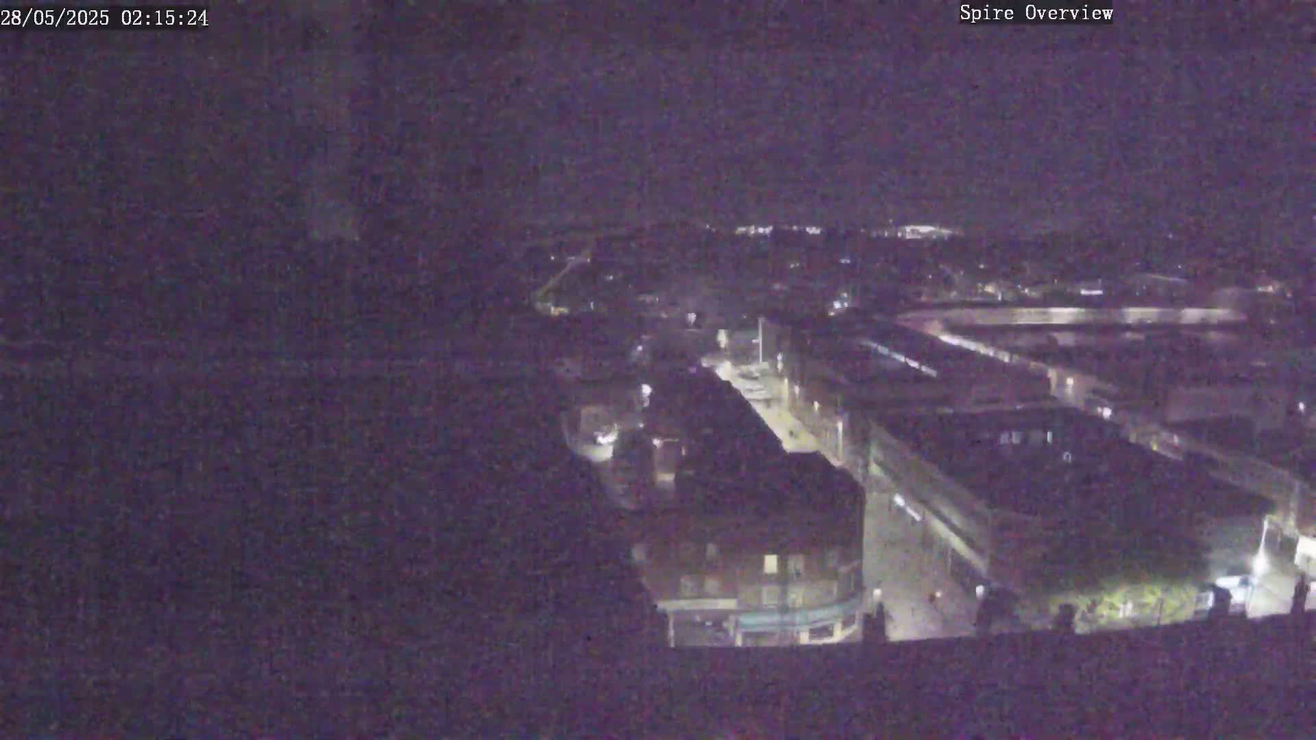 A nighttime, high-angle view shows a city block with dimly lit buildings and streets.