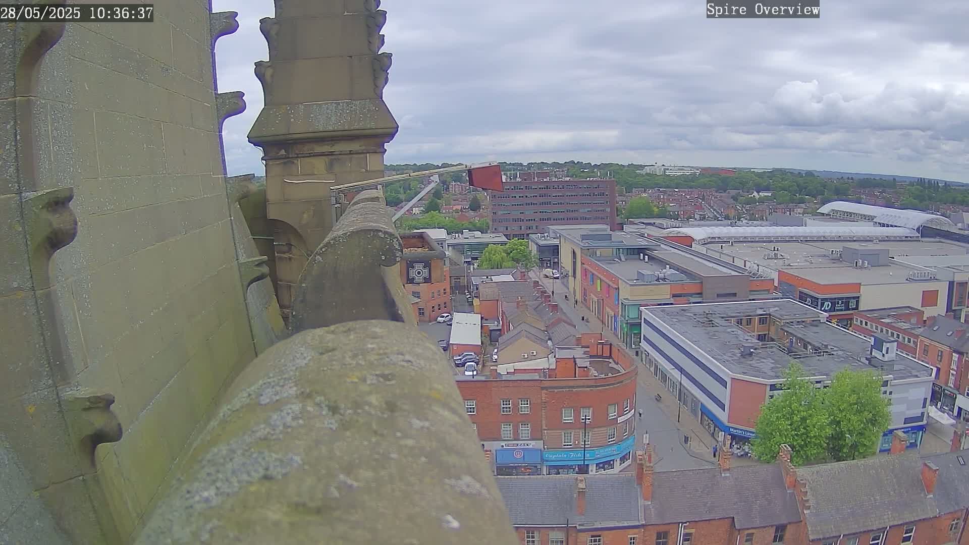 A high-angle view from a stone structure shows a town square with buildings under a partly cloudy sky.