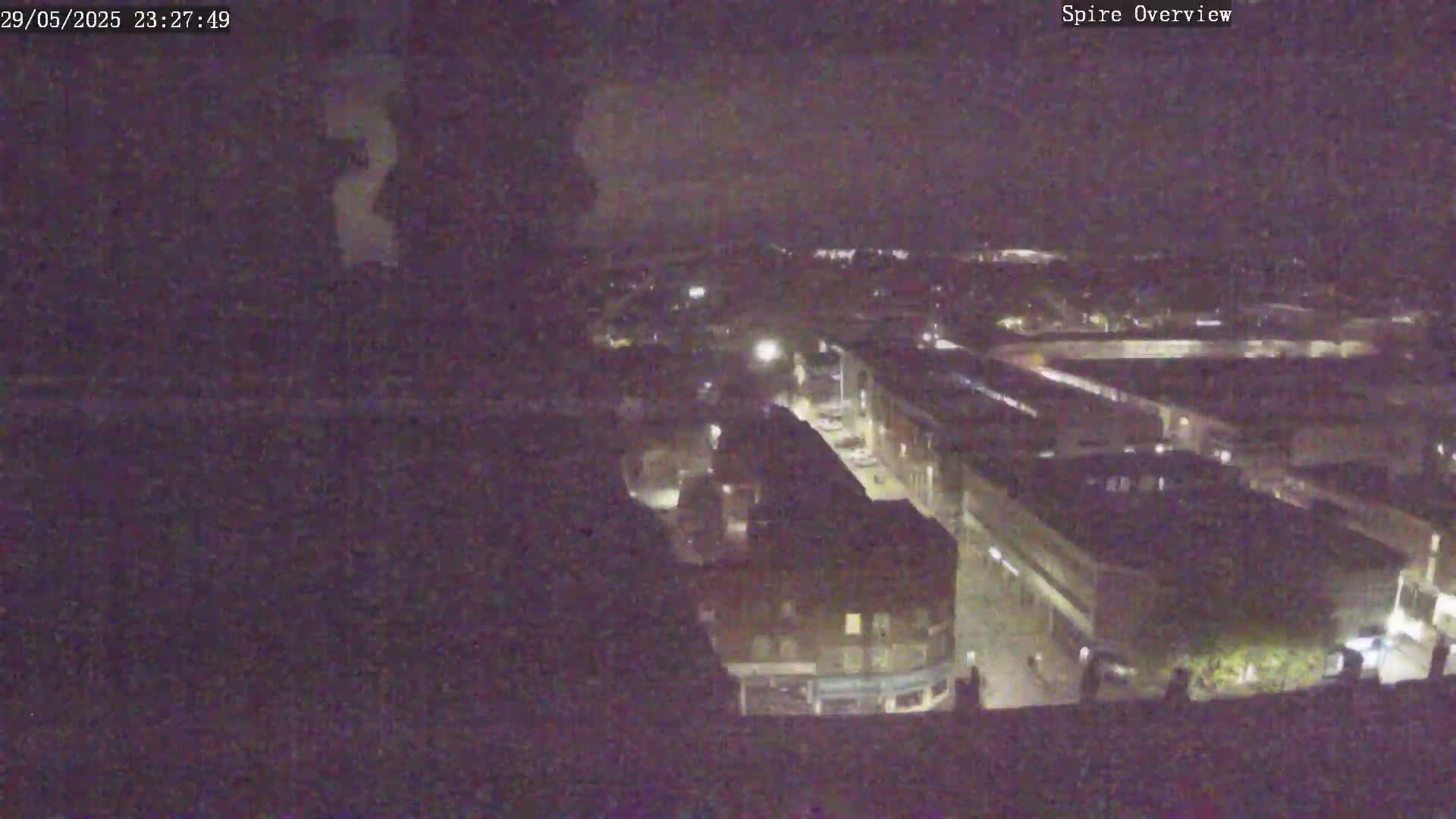 A nighttime, high-angle view shows a town or city with dimly lit buildings and streets.