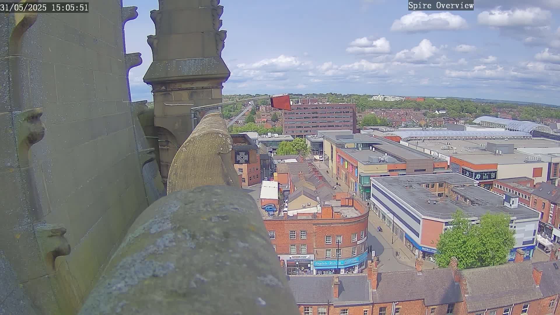 A high-angle view from a stone structure shows a town square on a partly cloudy day.