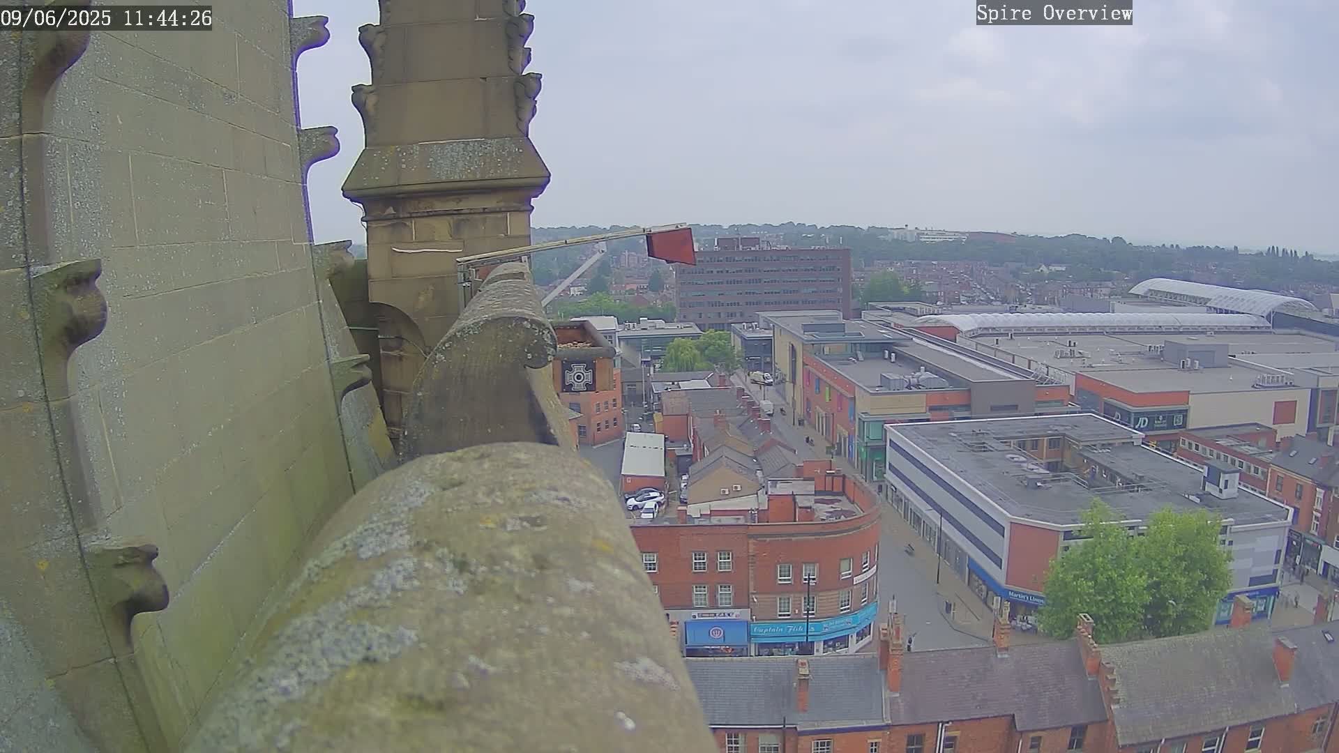 A high-angle view from a stone structure on an overcast day shows a town square with buildings and a shopping mall.