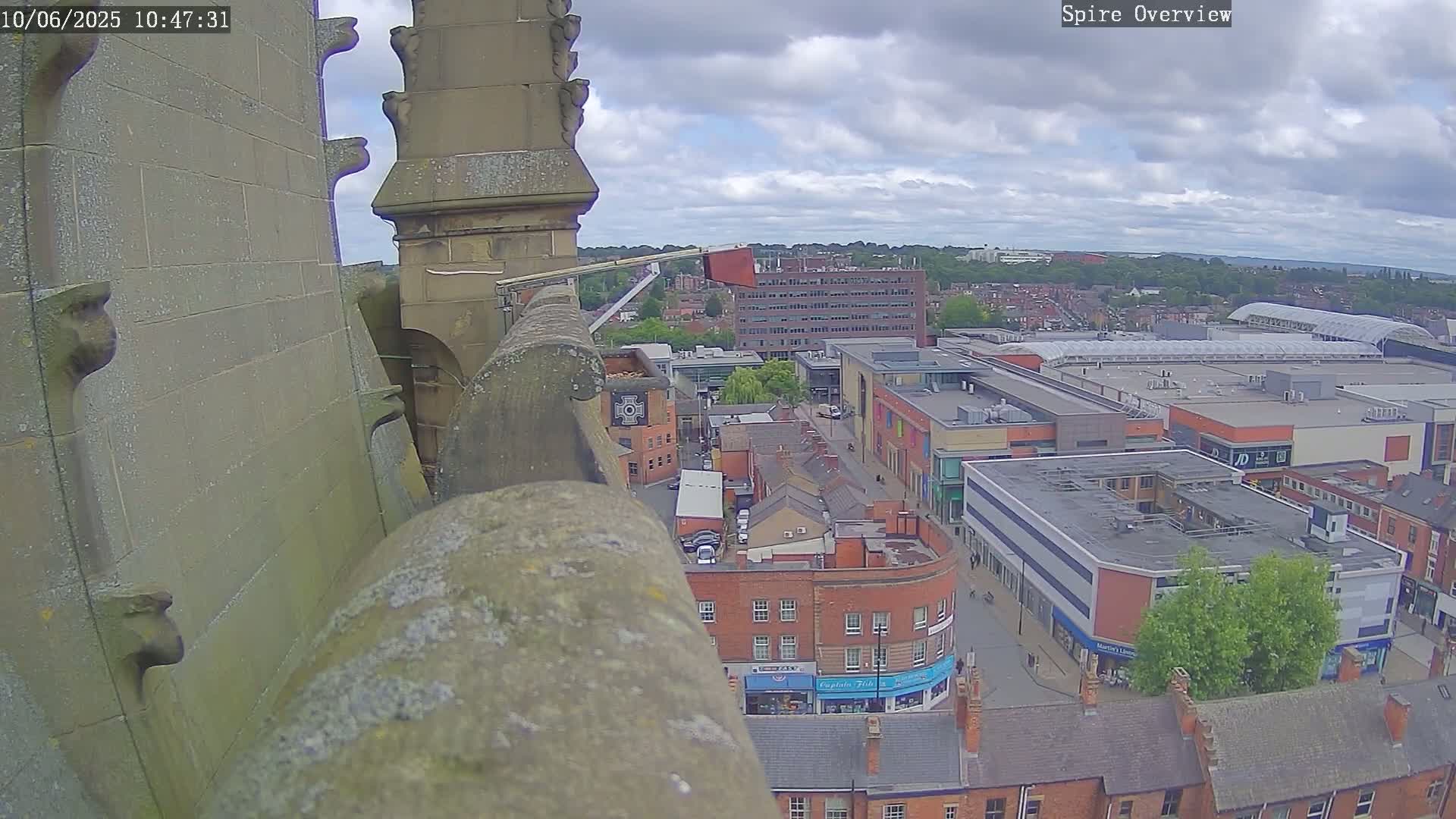 A high-angle view from a stone structure shows a town under a partly cloudy sky, with a shopping center and numerous brick buildings visible.
