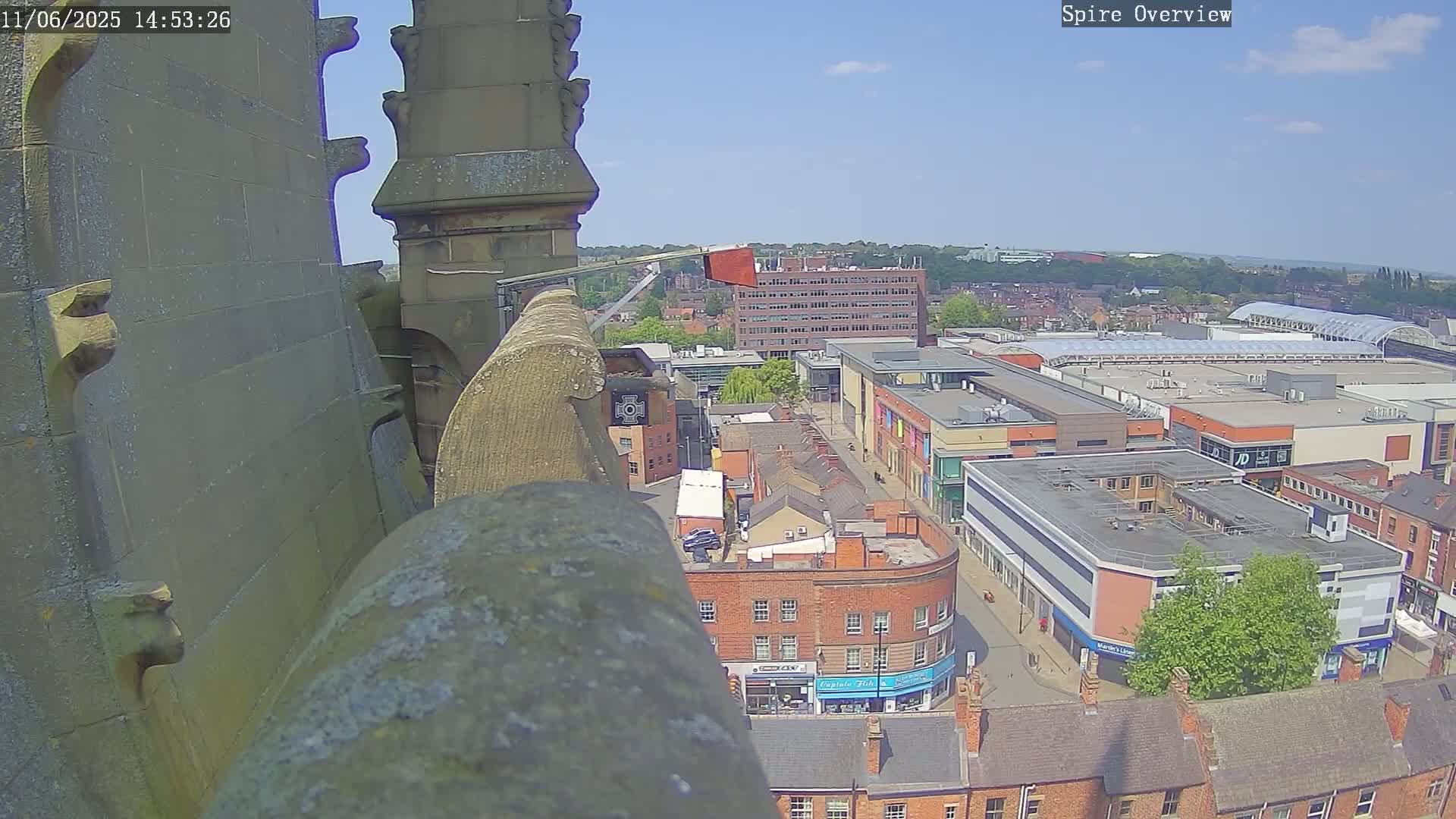 A high-angle view from a stone structure shows a town on a sunny day, with a shopping center and other buildings visible.