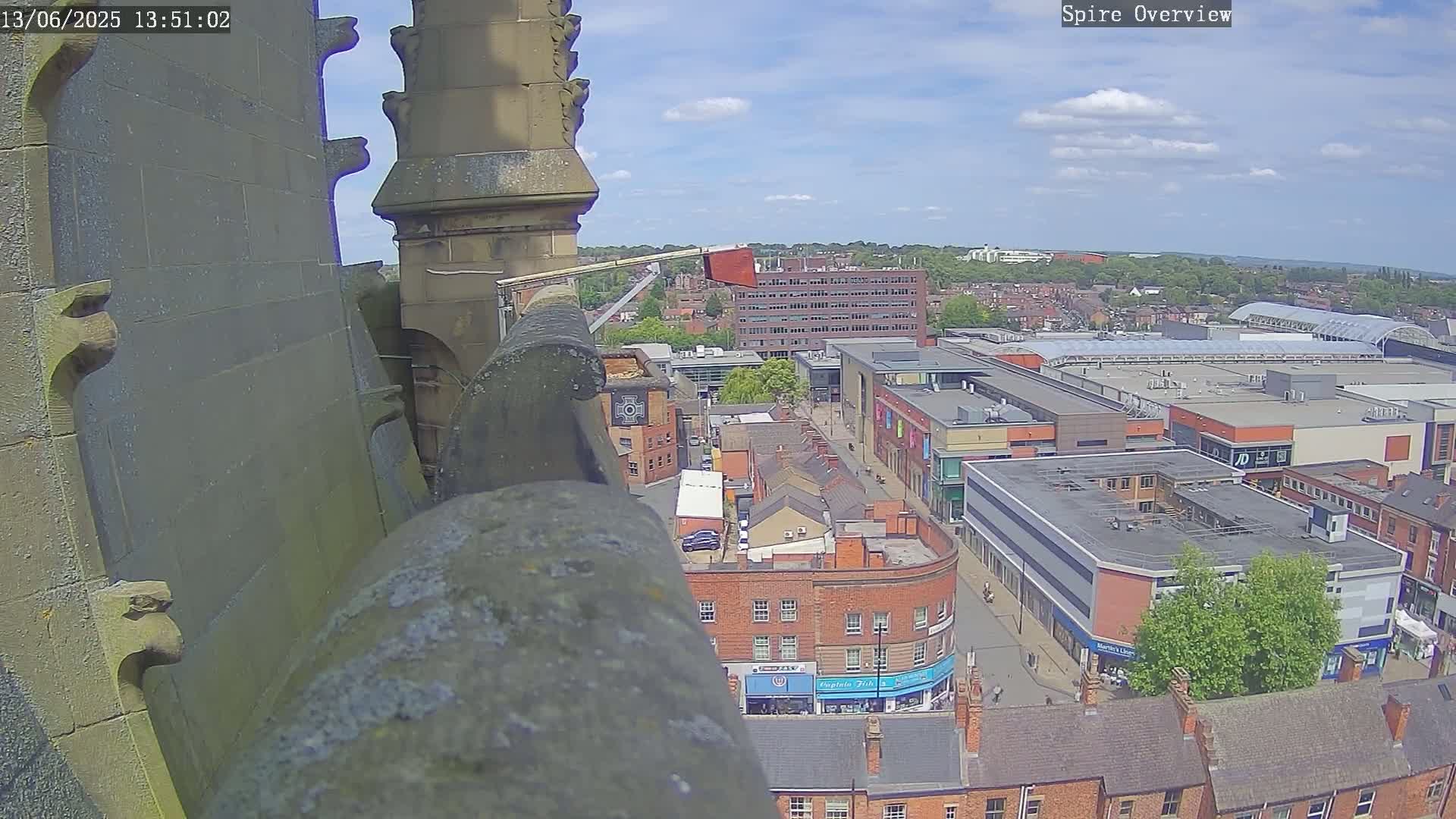 A high-angle view from a stone structure shows a partly sunny day over a city with a shopping center and many brick buildings.