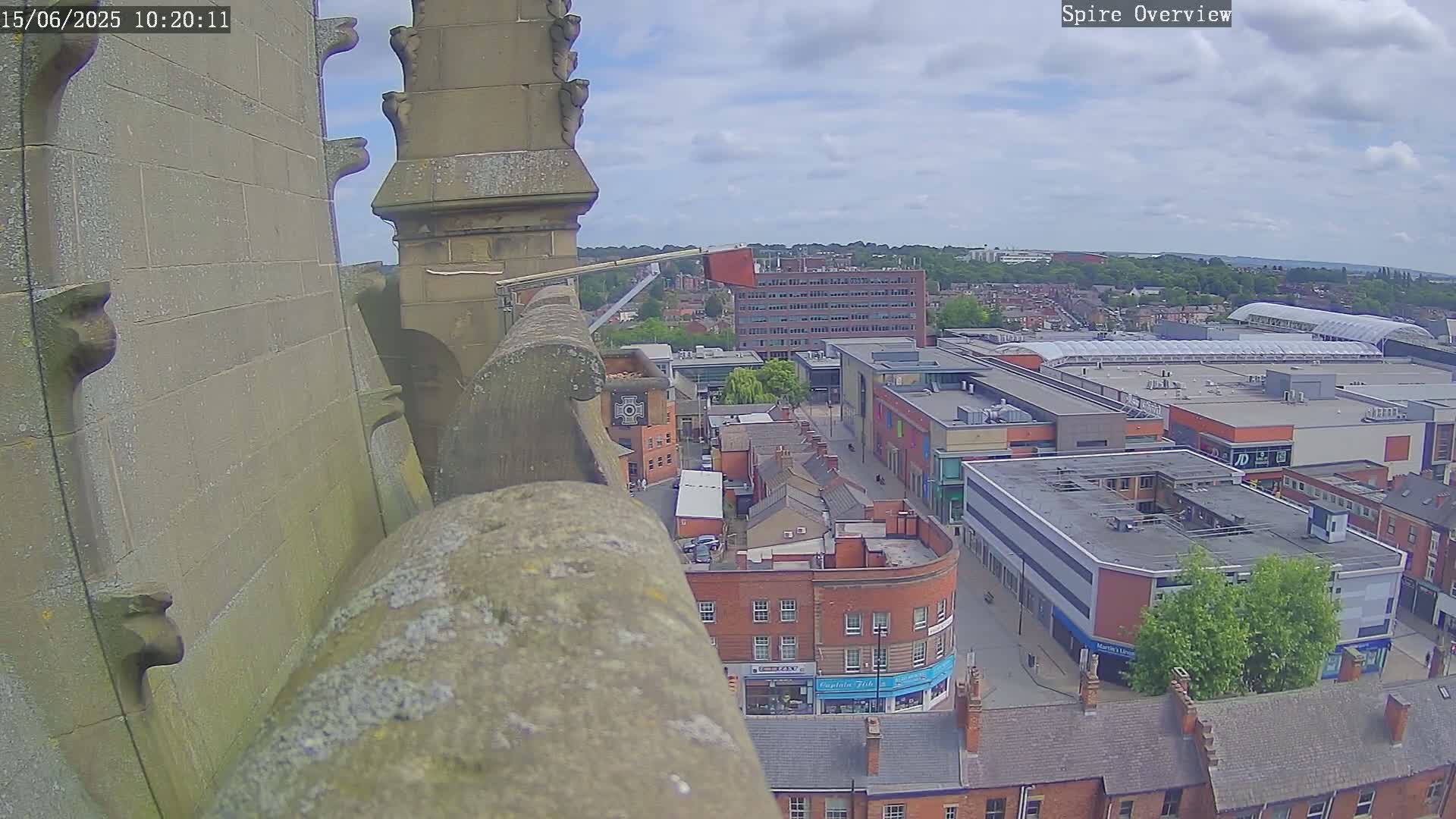 A high-angle view from a stone structure on a partly cloudy day shows a town square with shops and buildings below.