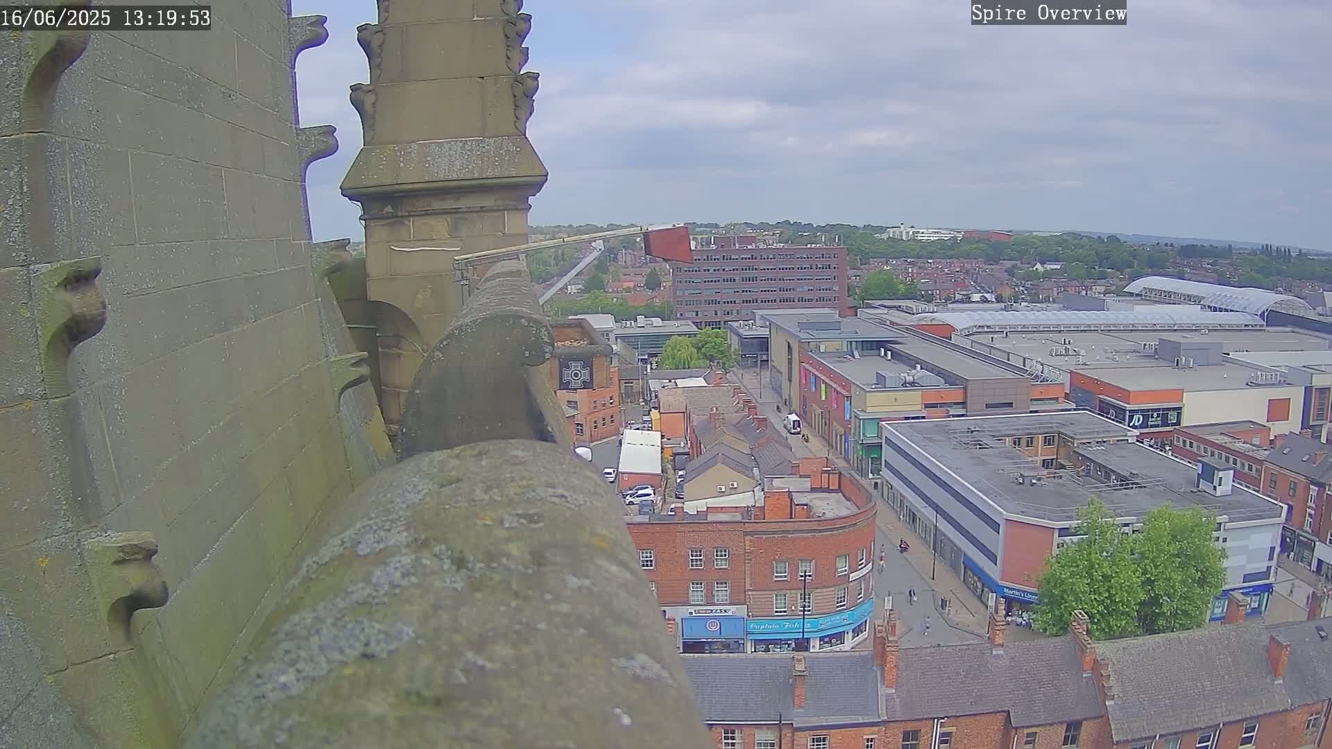 A high-angle view from a stone structure shows a town square with multiple buildings under a partly cloudy sky.