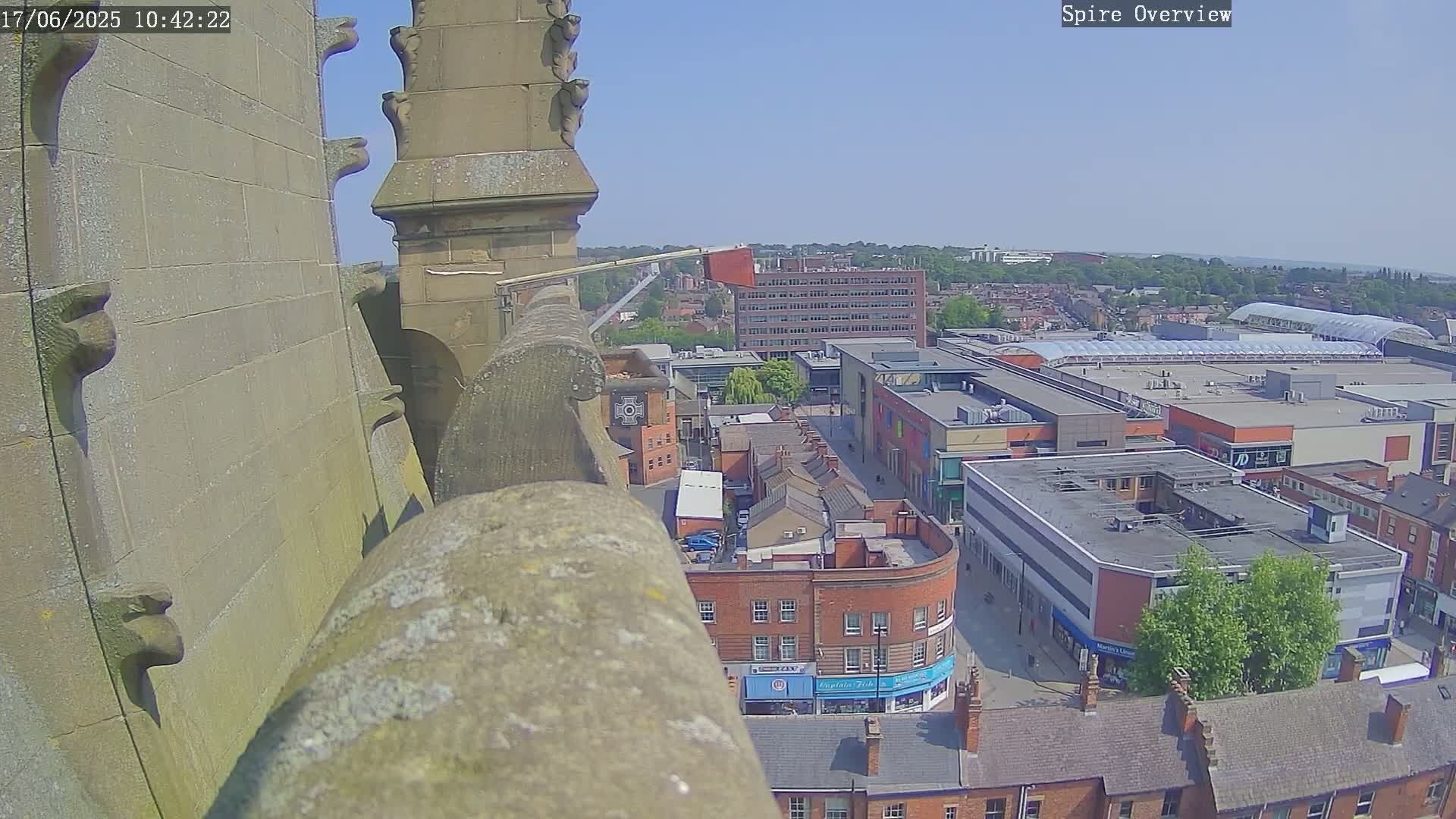 A high-angle view on a sunny day shows a stone structure overlooking a town square with brick buildings and a large shopping center.