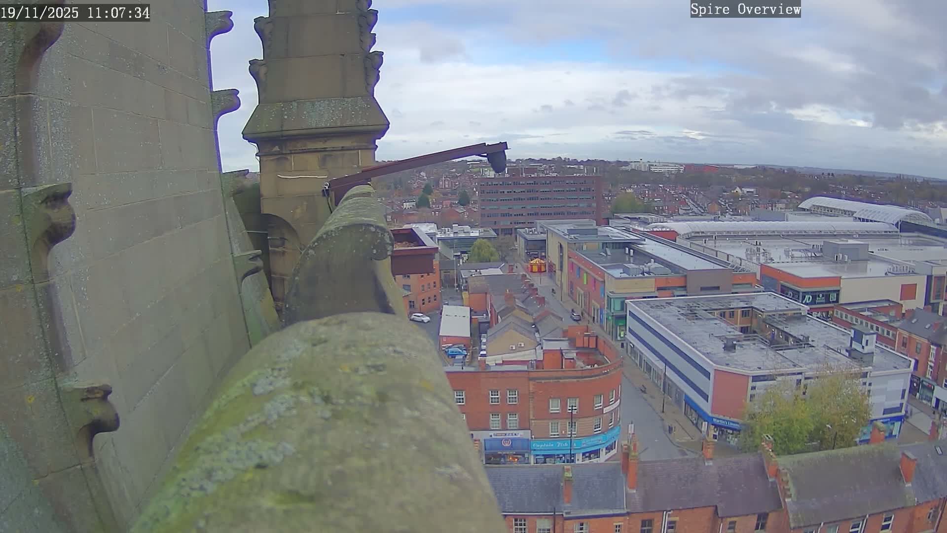 A high-angle view from a stone structure shows an overcast day over a city with brick buildings and a large shopping center.
