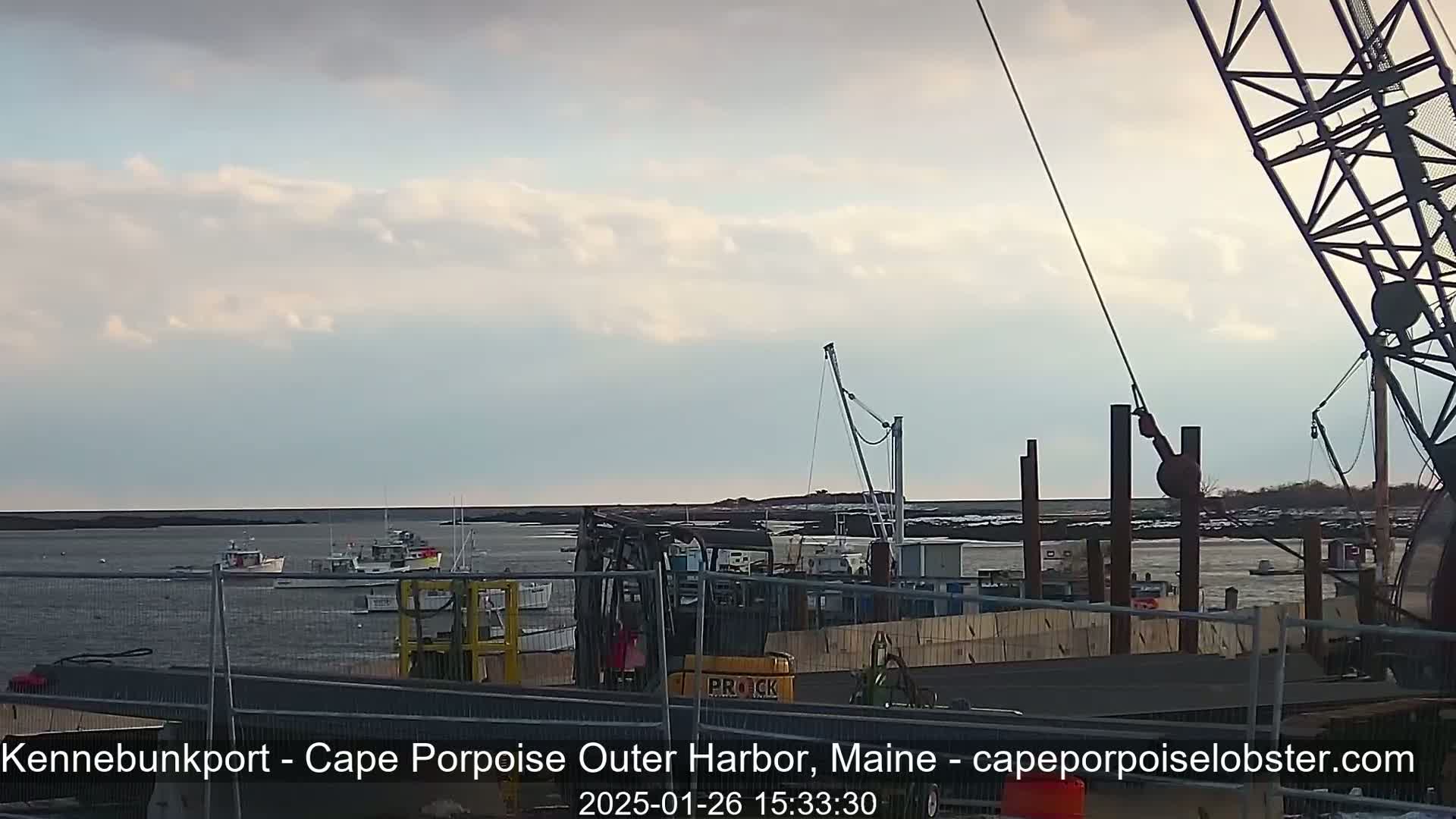 Here's a description of the image:  A harbor scene under a partly cloudy sky shows several fishing boats in the water and construction equipment on the dock.