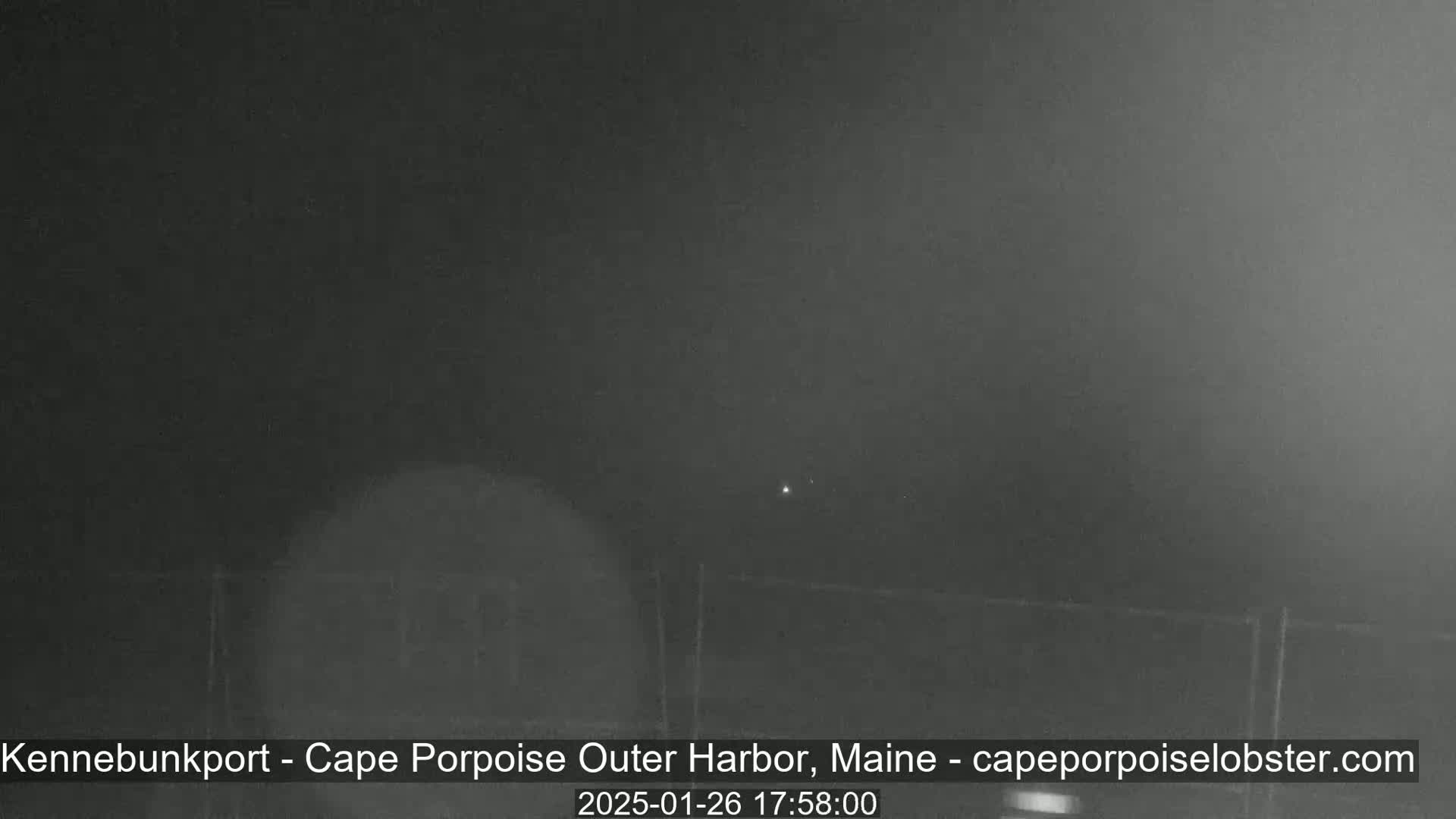 A dark, nighttime outdoor scene shows a blurry, indistinct view of a possibly foggy harbor.