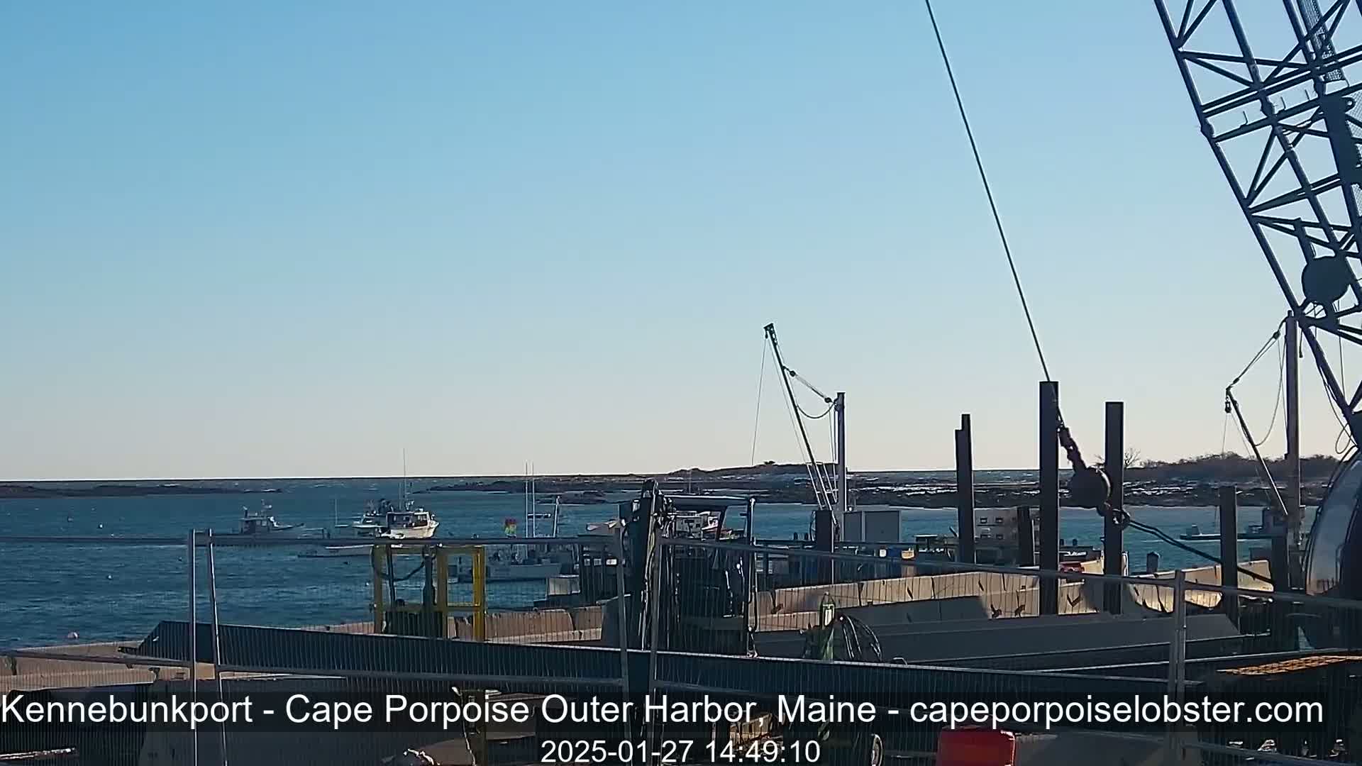 A harbor scene on a clear day shows several boats moored near a construction site with a crane.