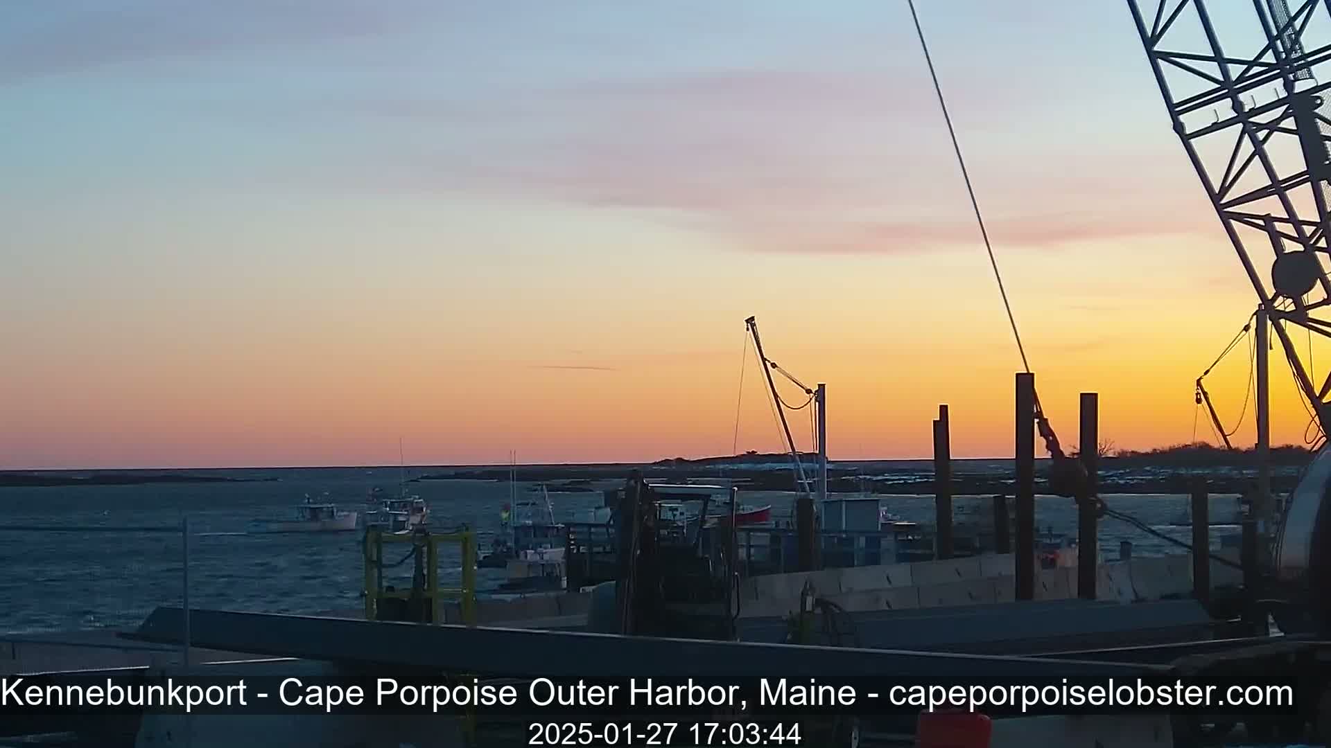 Several fishing boats are moored in a harbor at sunset under a clear, pastel sky.