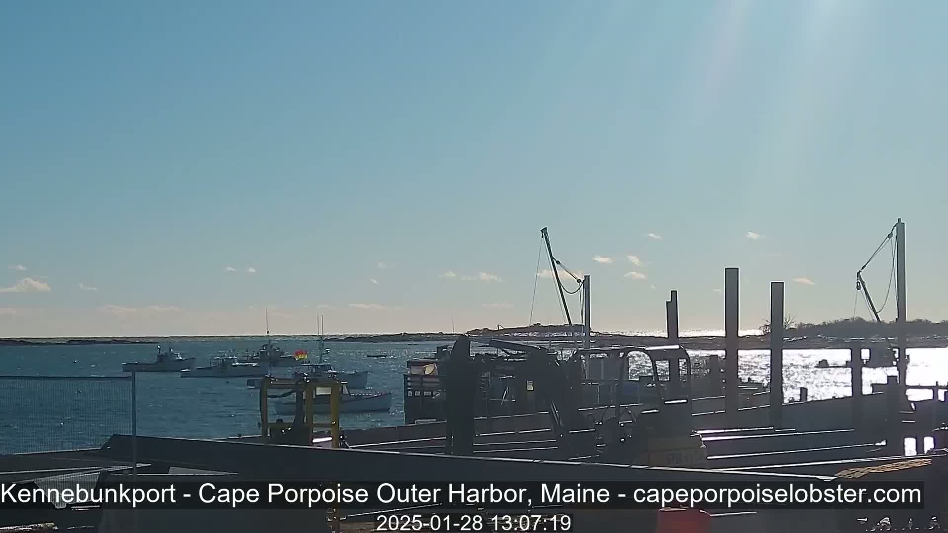 Several boats are moored in a harbor on a sunny day with a mostly clear sky.