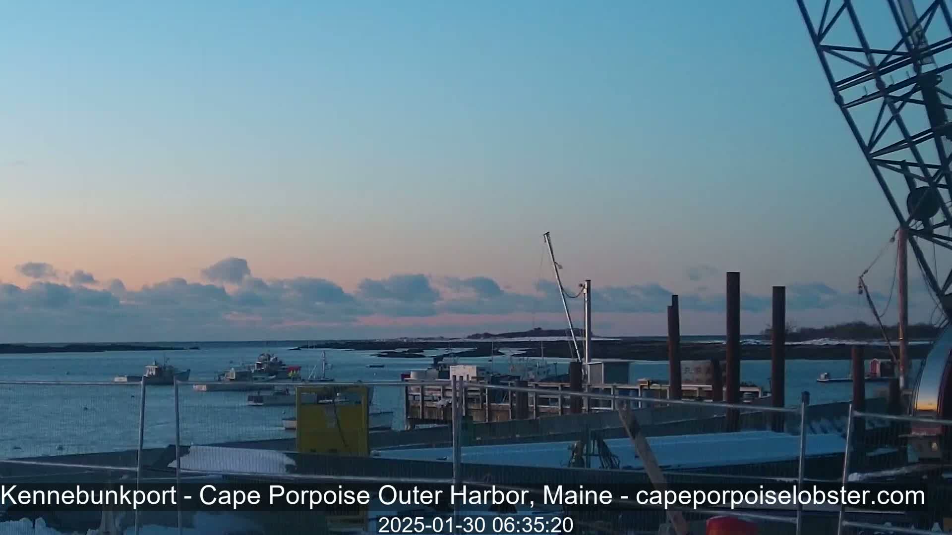 Several fishing boats are moored in a harbor at dusk under a mostly clear sky with a few scattered clouds.