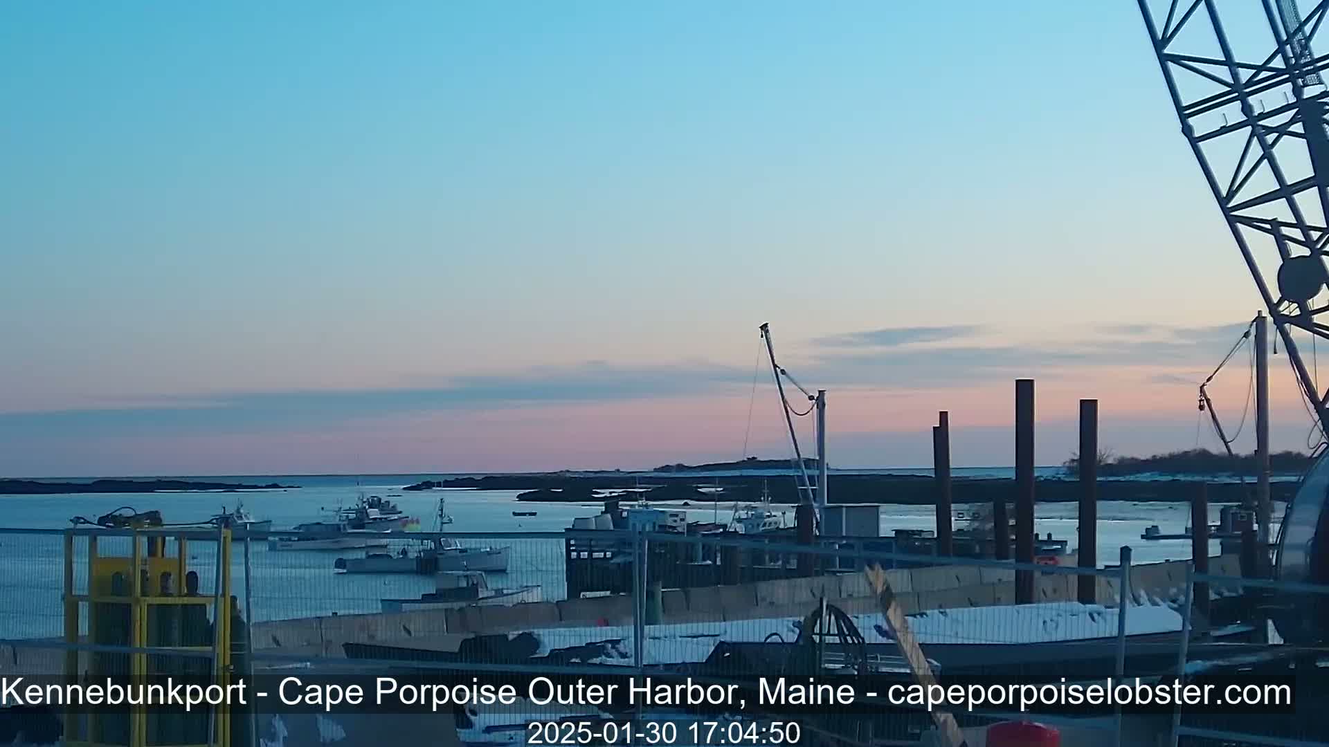 Several boats are moored in a harbor at dusk under a clear, pastel sky.