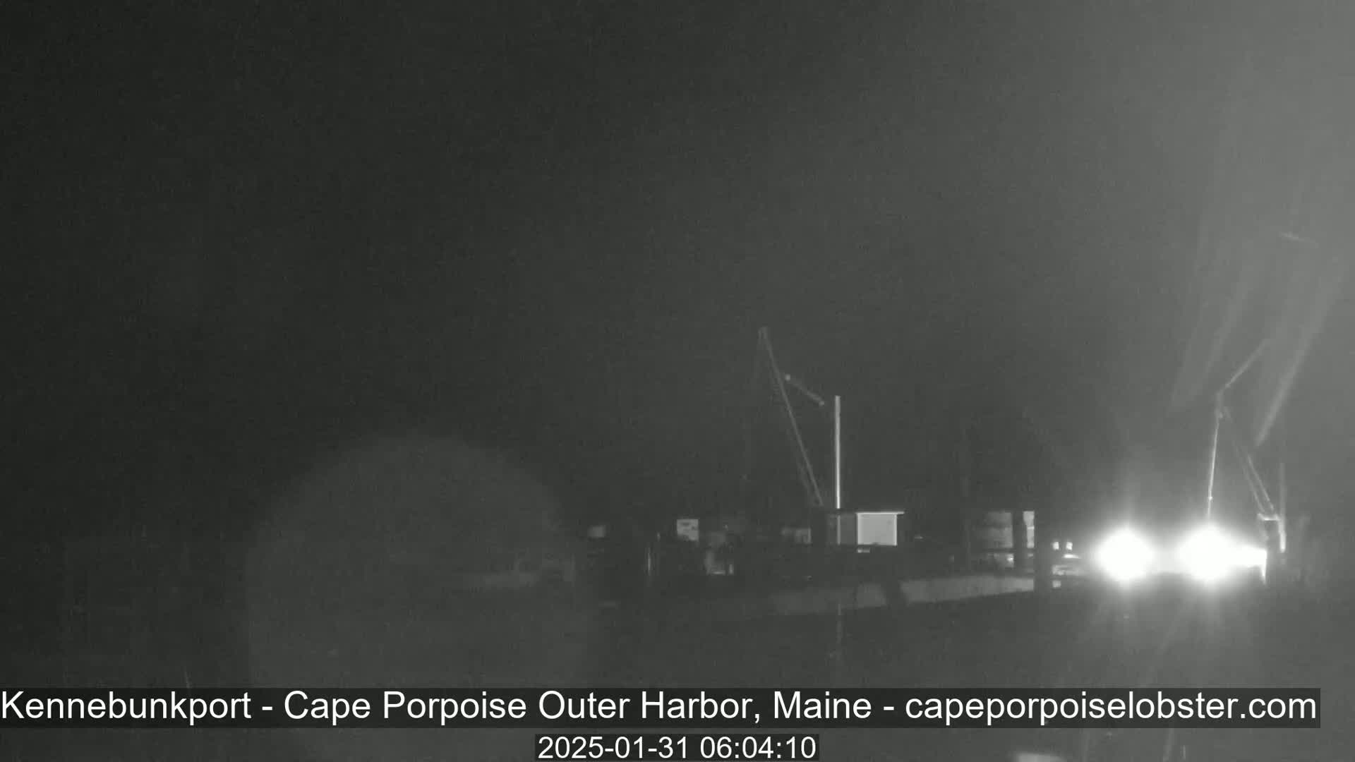 A nighttime, foggy view of a harbor with two cranes and bright lights.