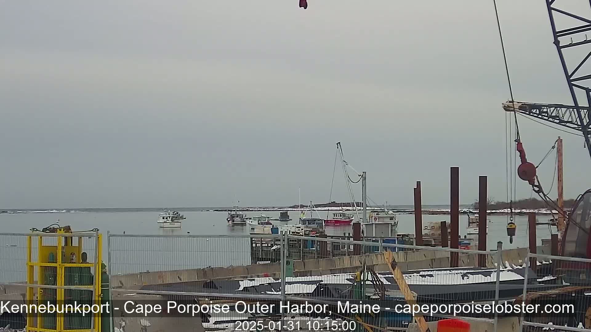 Several boats are moored in a harbor under an overcast sky, with some construction or maintenance work underway on the dock.