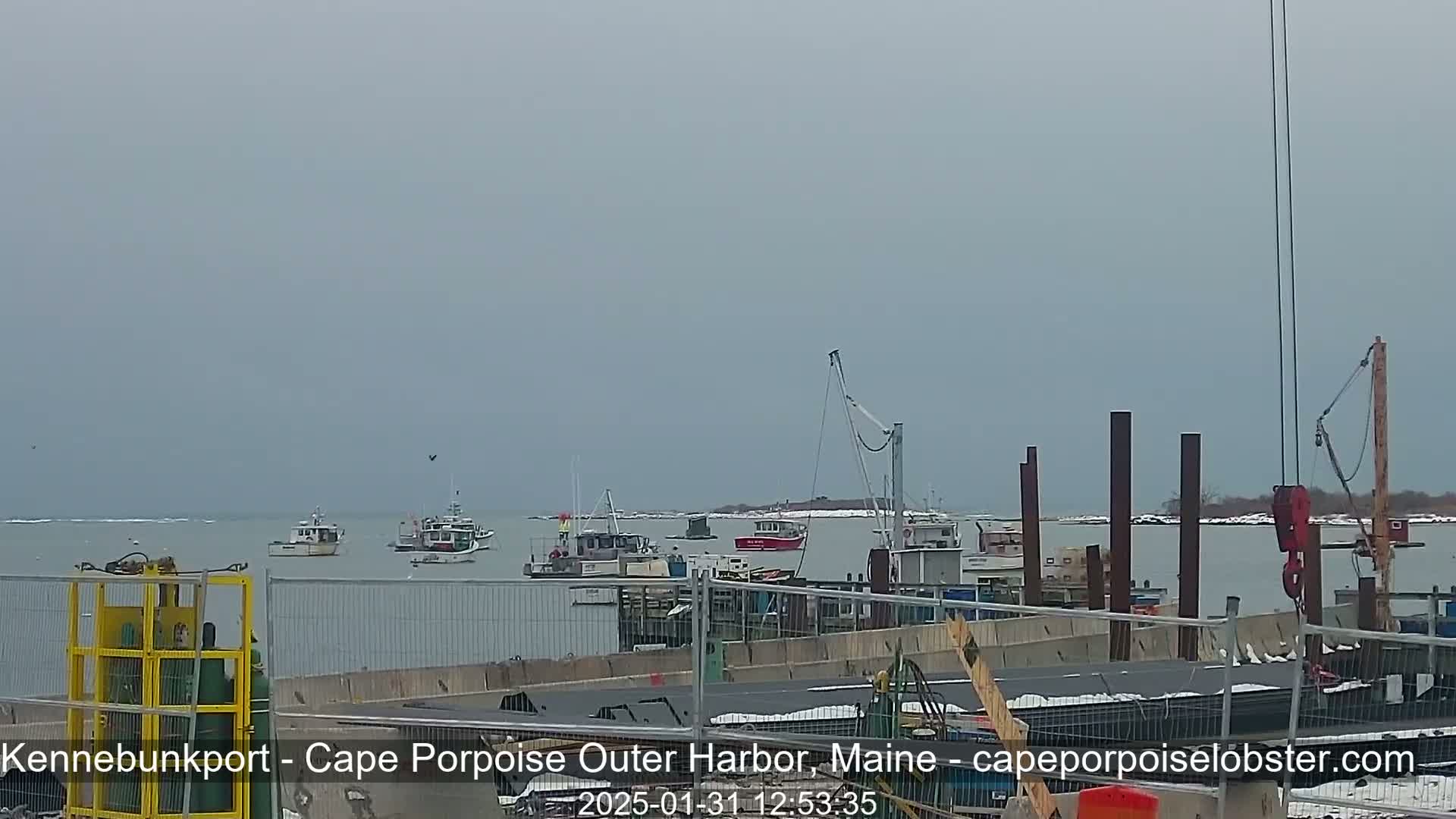 Several fishing boats are moored in a harbor on an overcast day, with construction underway at a nearby dock.