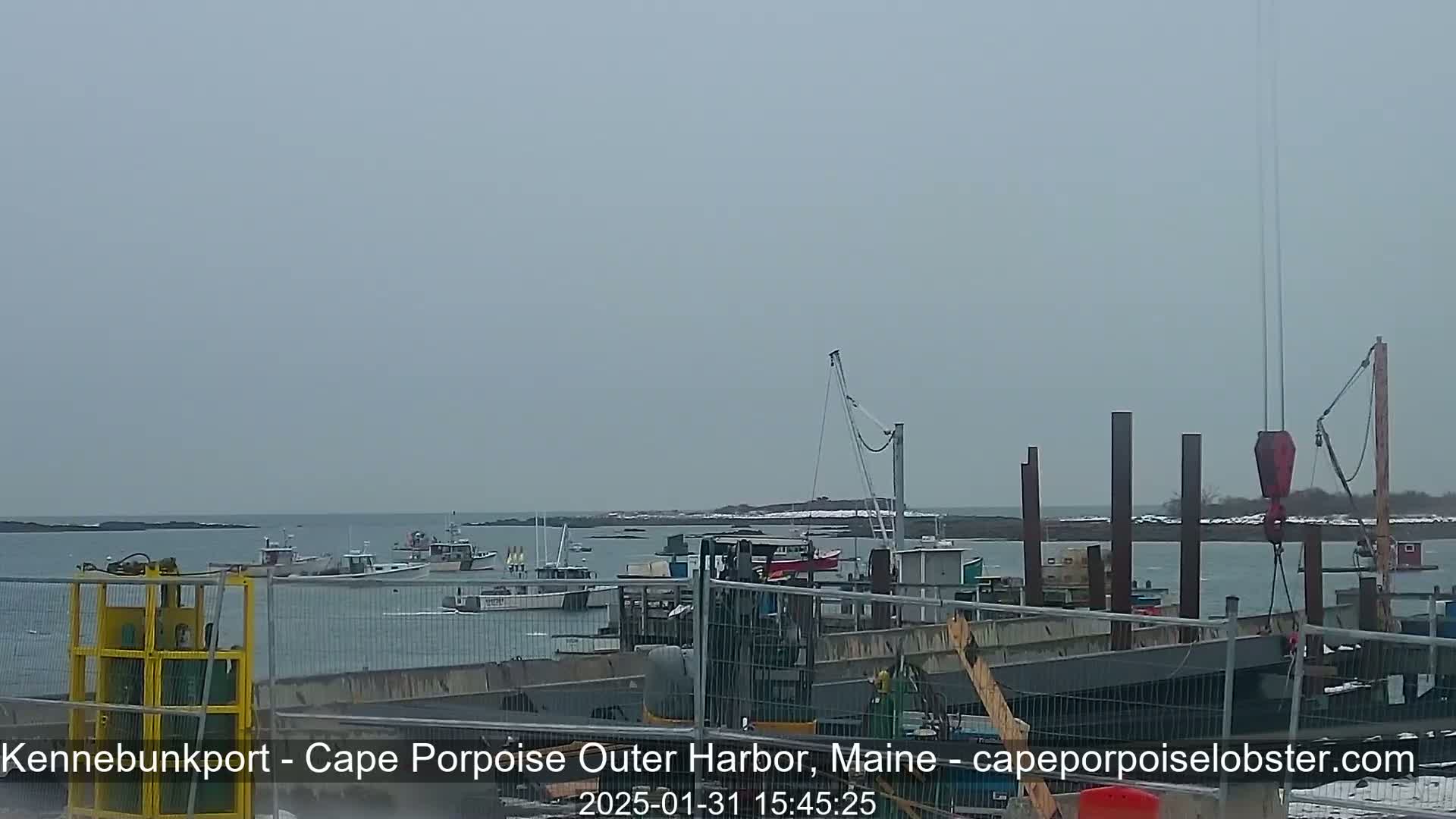 Several boats are moored in a harbor under an overcast sky, with construction underway on a pier in the foreground.
