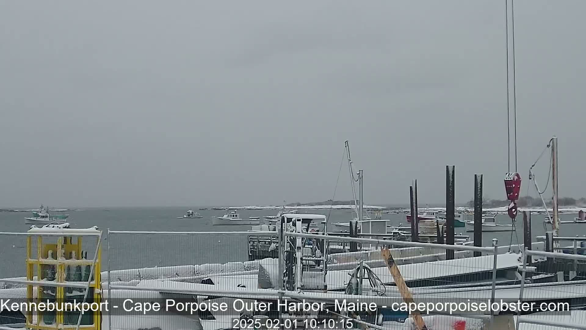 A snow-covered harbor scene shows several boats moored at a dock, with a forklift and other equipment also covered in snow.