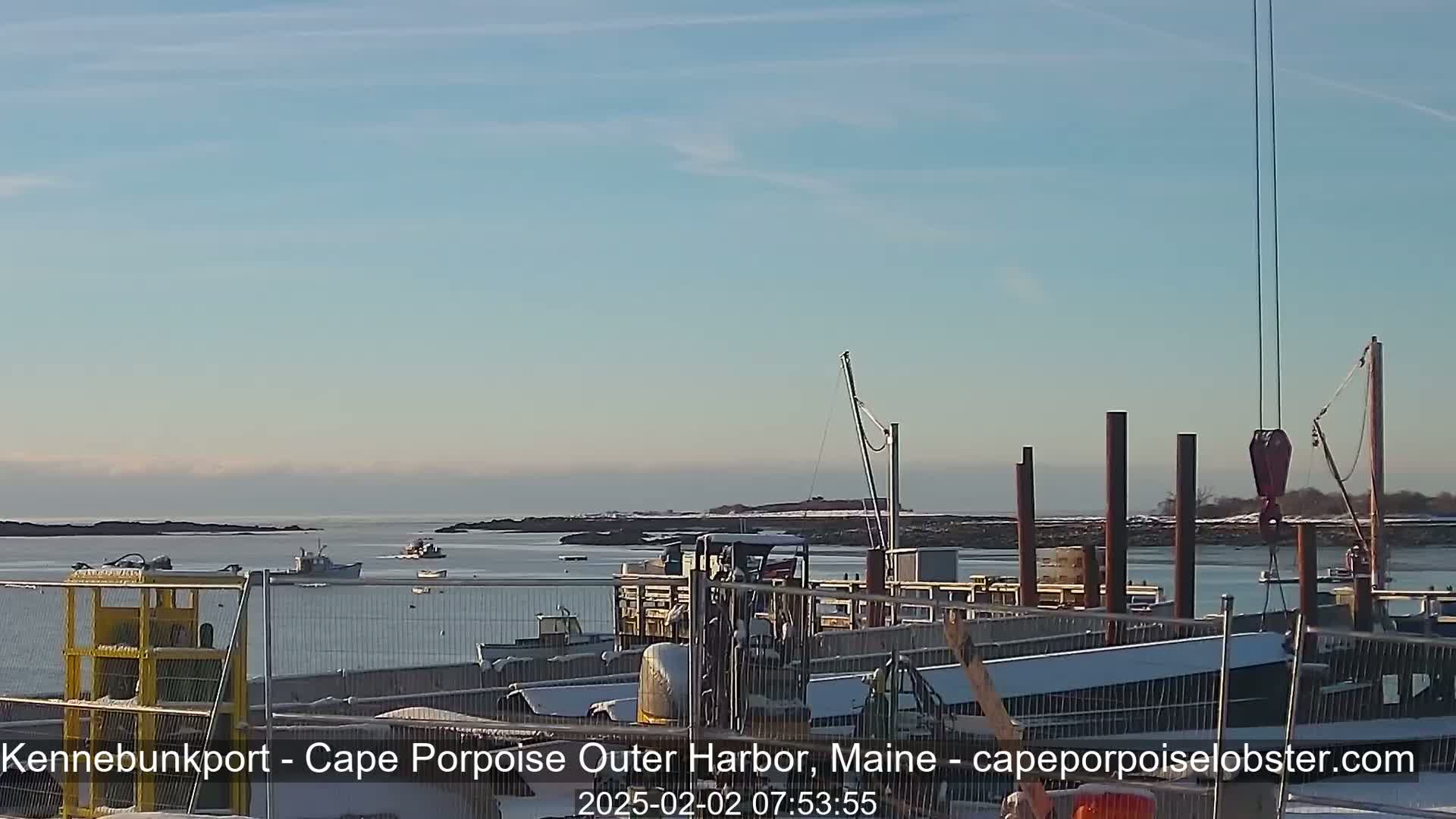 A harbor with several boats, construction equipment, and a crane is visible under a clear, light blue sky; some snow is on the ground.