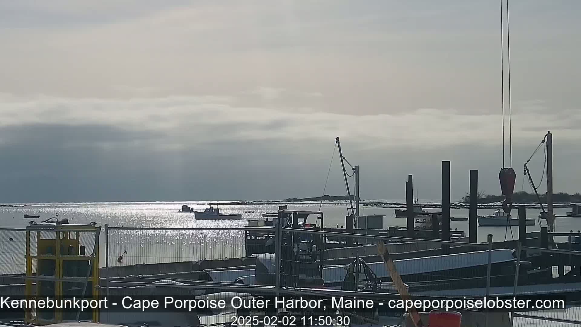 A harbor scene under a cloudy sky shows several boats near a dock with construction materials and equipment.