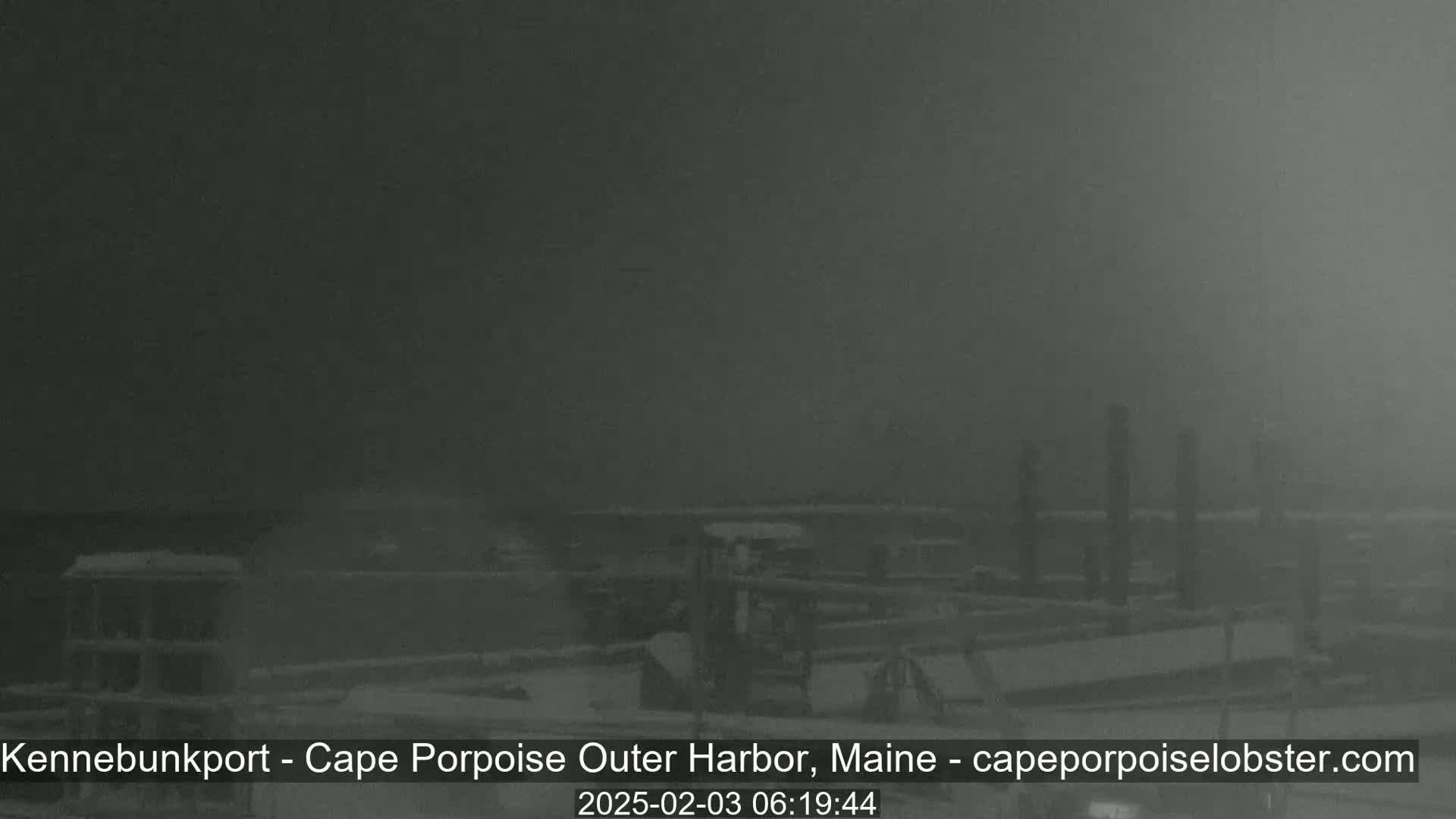 A foggy harbor scene shows a snow-covered dock and several dark structures under a dim sky.