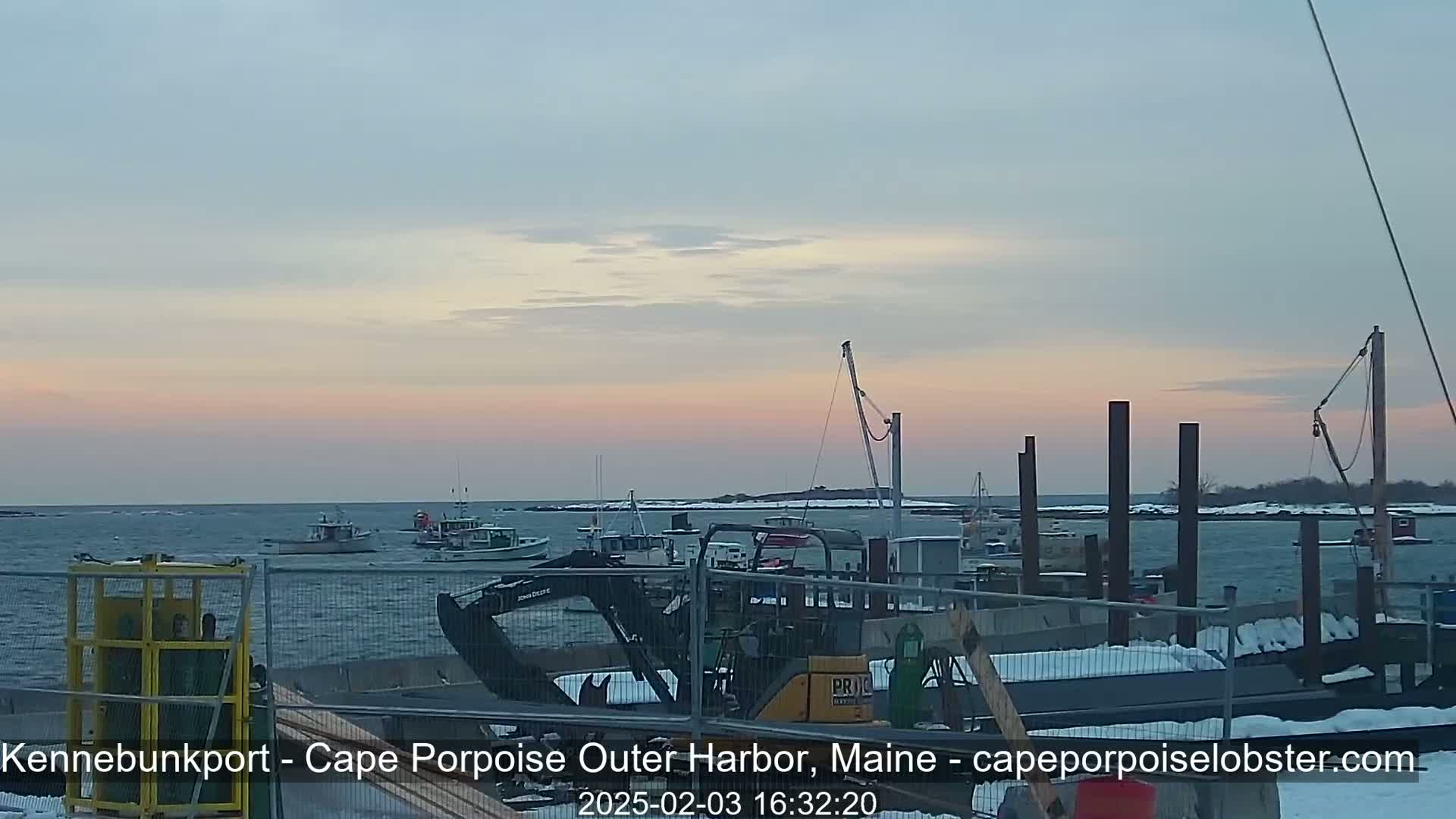 Several fishing boats are moored at a harbor under a pale, pinkish sunset sky.