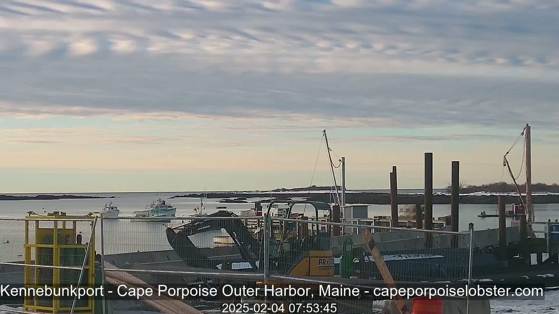 A partly cloudy, cool day at a harbor with several boats, construction equipment, and temporary fencing.