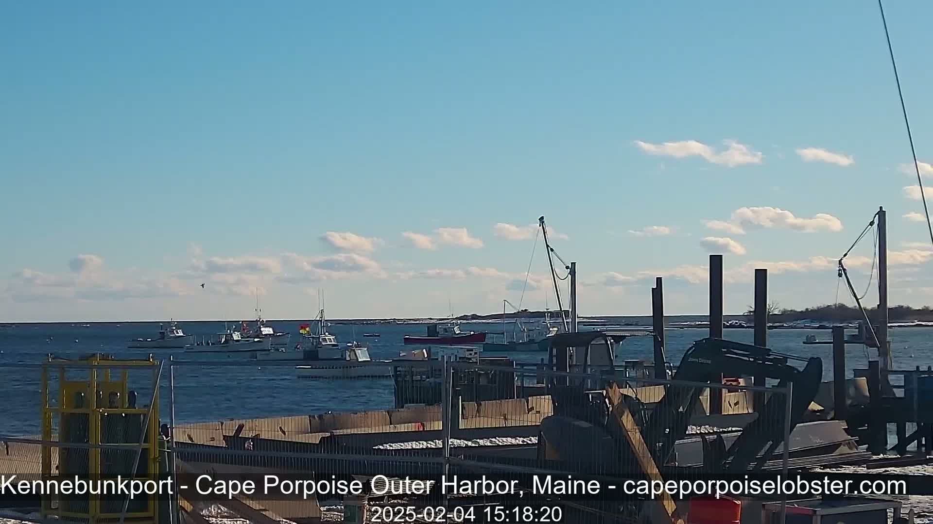 Several fishing boats are at sea on a partly cloudy day, viewed from a harbor with construction equipment on a dock.