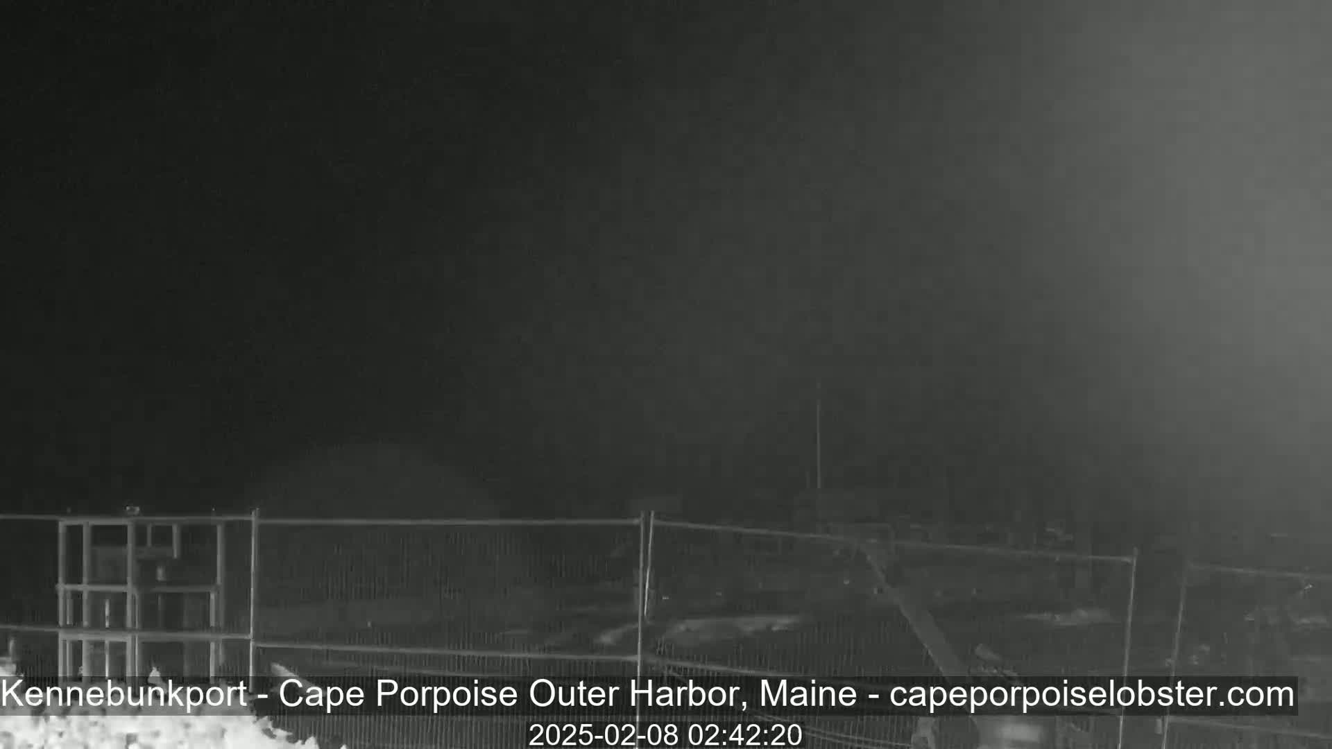 A nighttime, snow-covered scene shows a metal fence surrounding an indistinct area, possibly under construction.