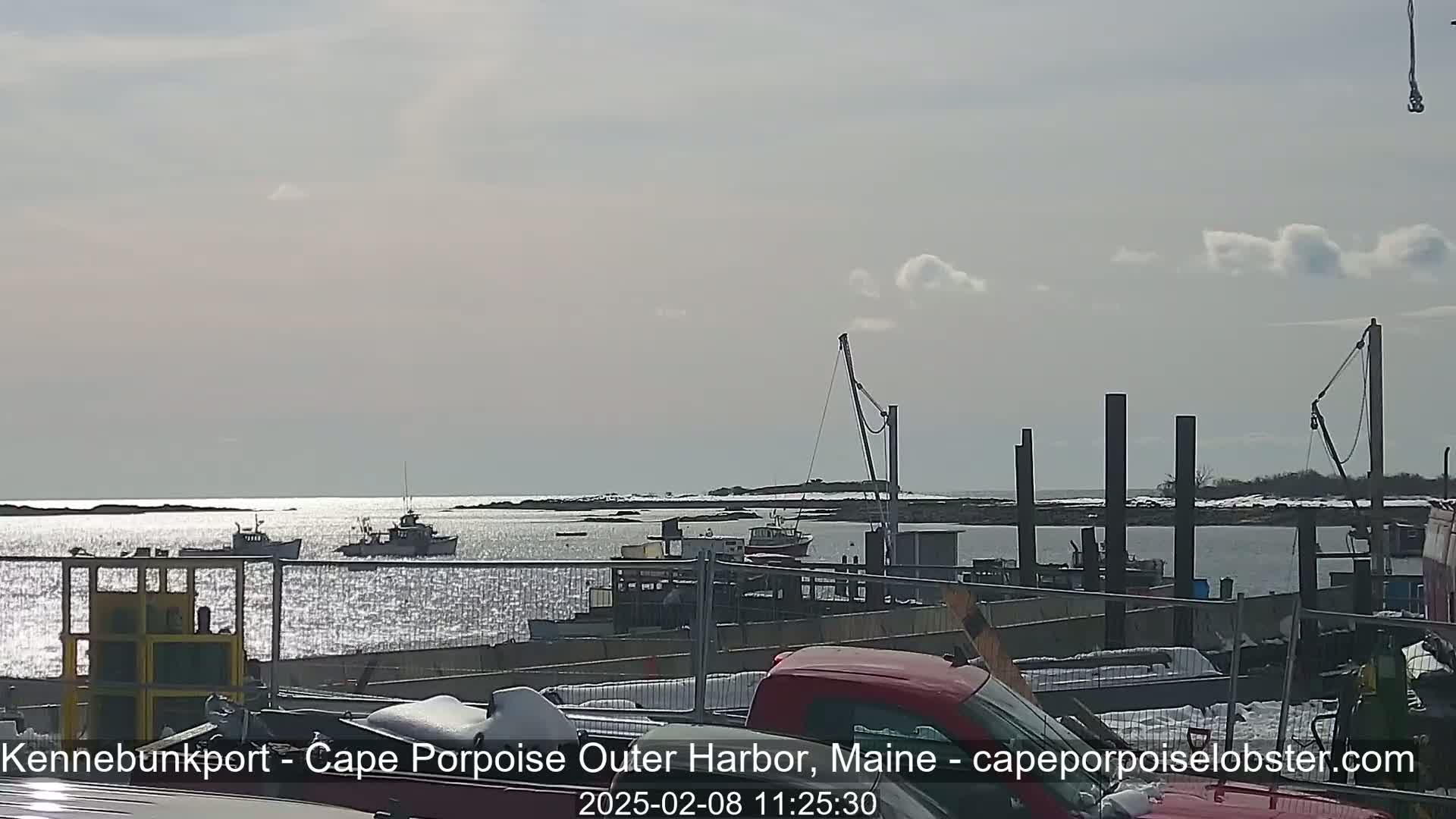 A harbor scene on a partly sunny day shows several boats moored near a dock, with additional boats visible further out in the water.