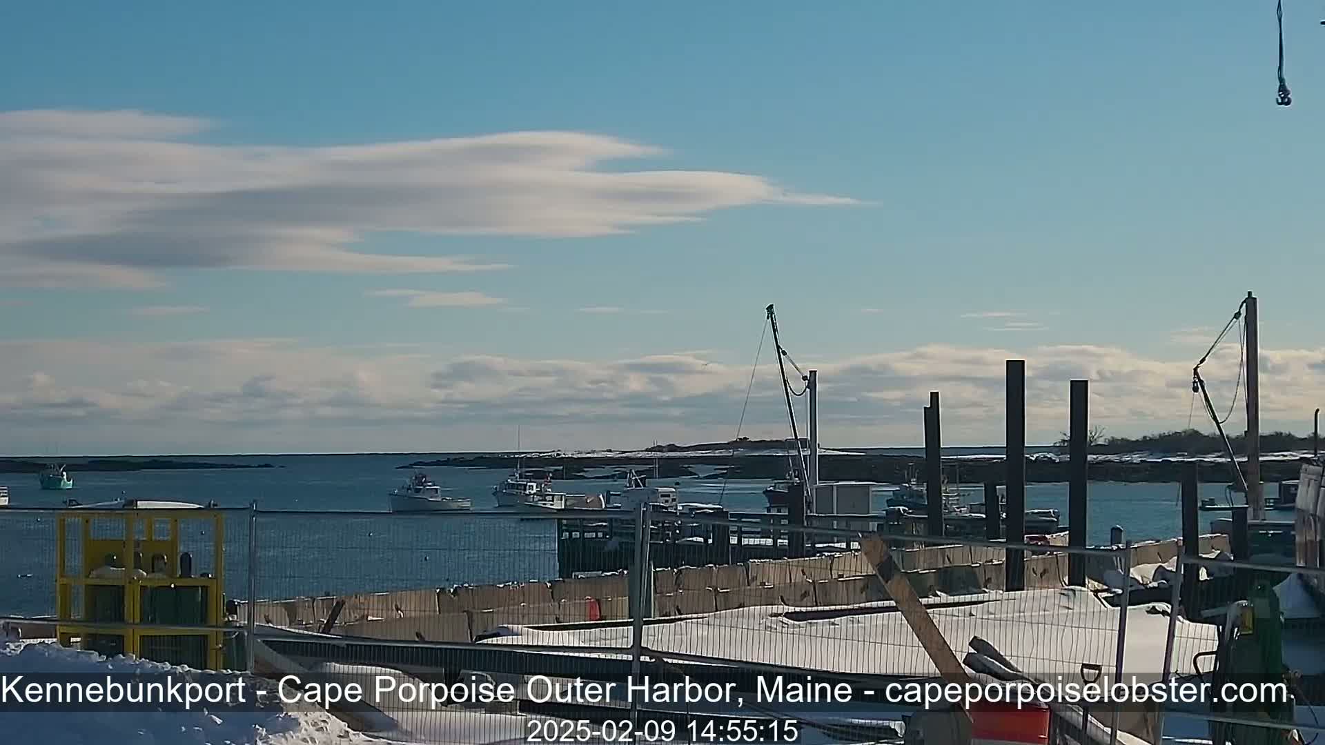 A harbor scene with several boats, a partially snow-covered dock undergoing construction, and a partly cloudy sky.
