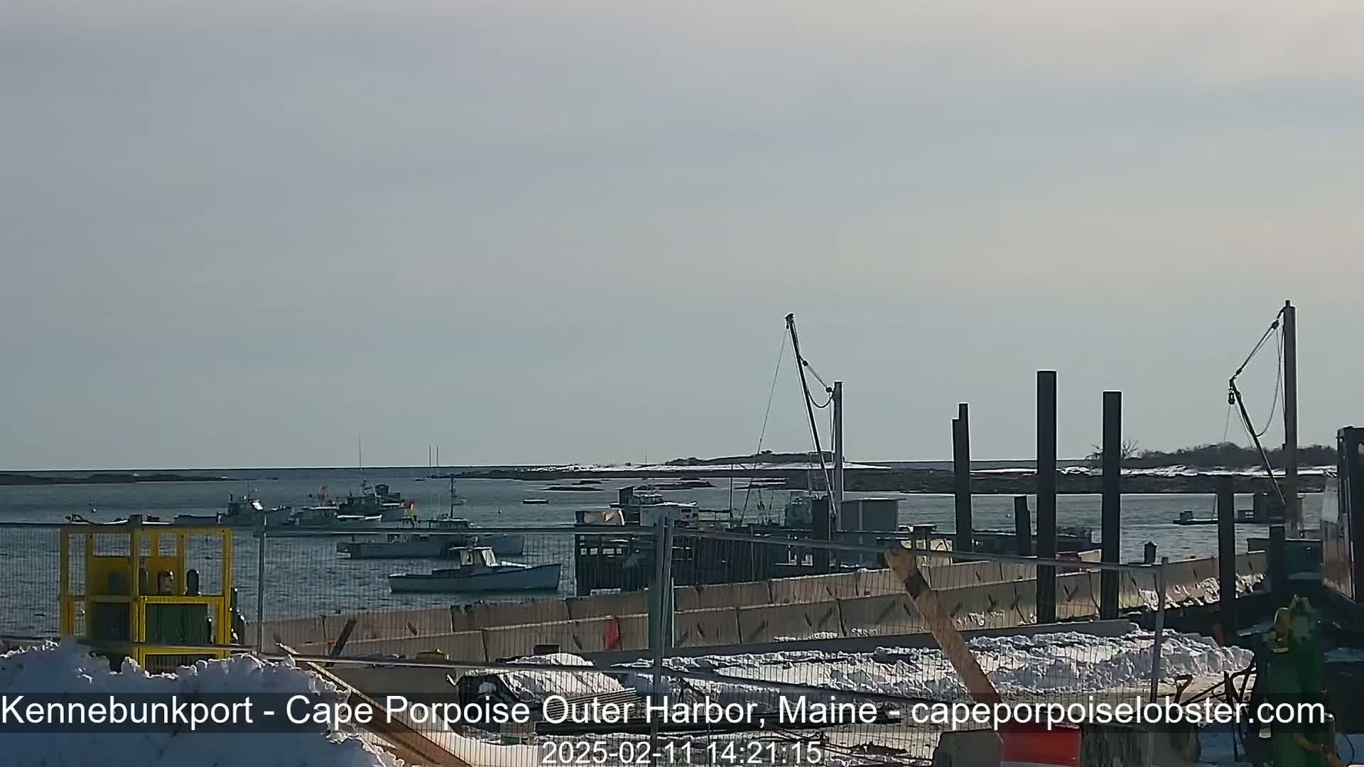 Several fishing boats are moored in a harbor on a partly sunny day with some snow on the ground.