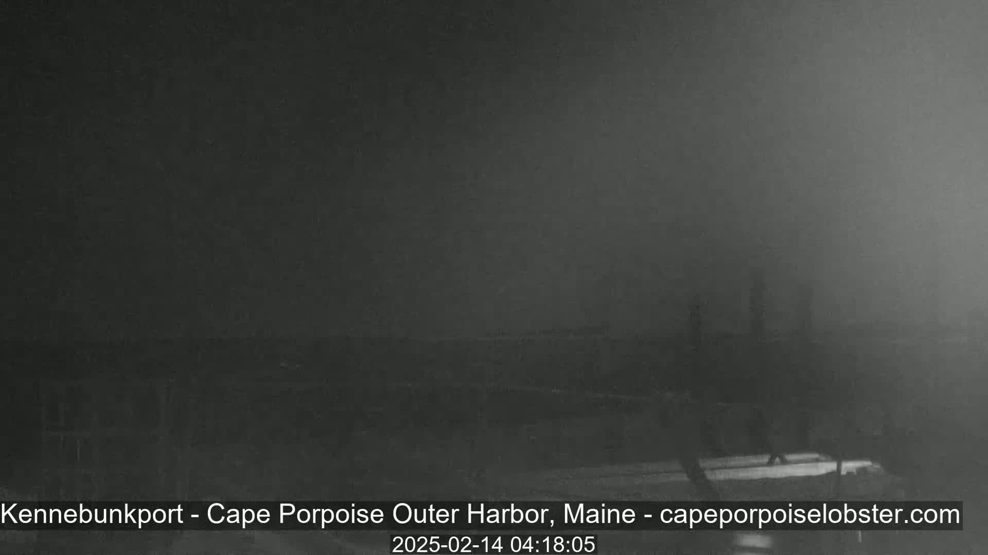 A dark, foggy scene shows indistinct shapes of what appears to be a harbor at night.
