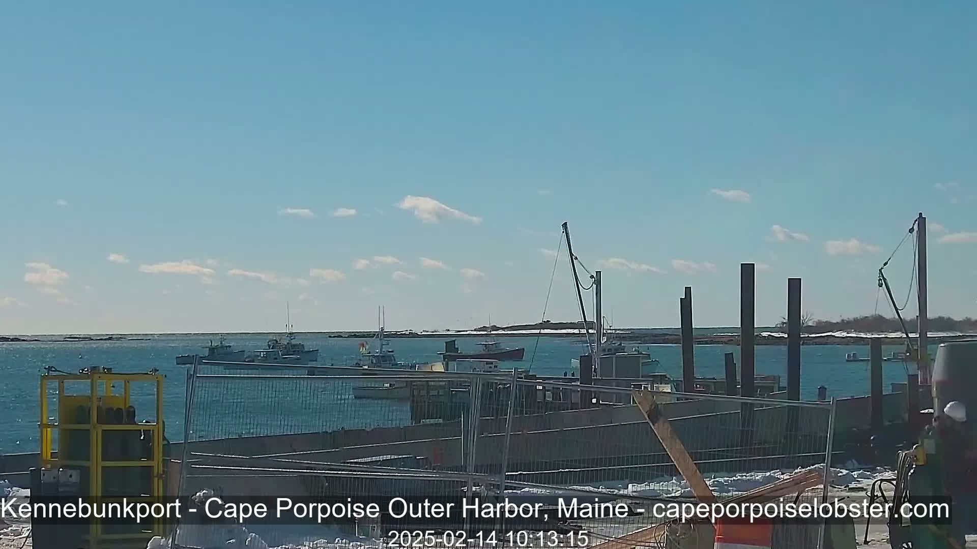 Several fishing boats are in a harbor on a partly sunny day with a clear blue sky and some snow on the ground.