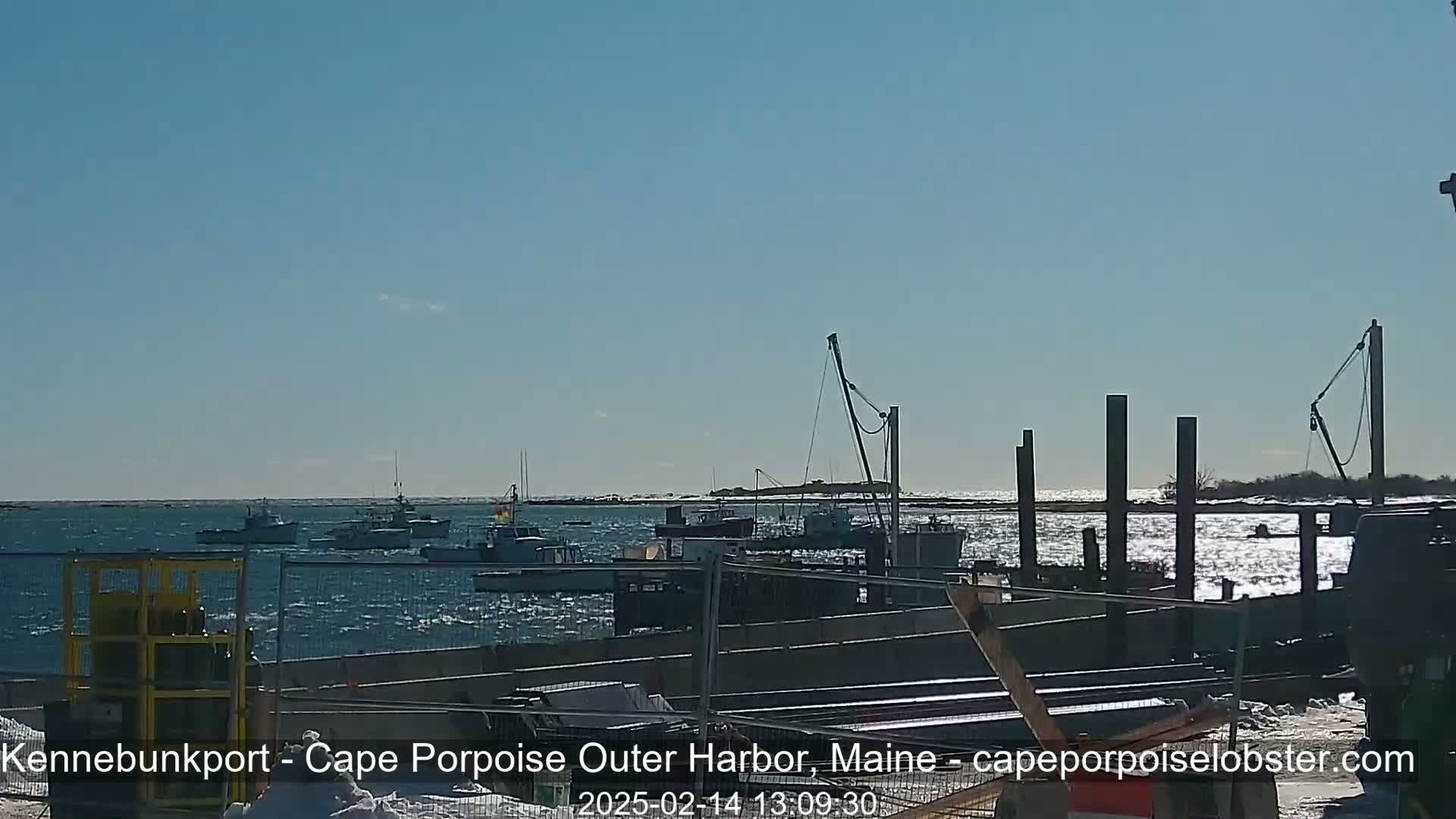 Several boats are in a harbor on a sunny day with a choppy sea.