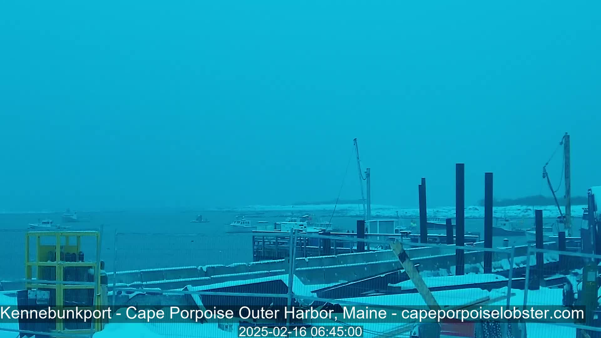 A snow-covered harbor with several boats and a crane is visible under a clear, light-blue sky.