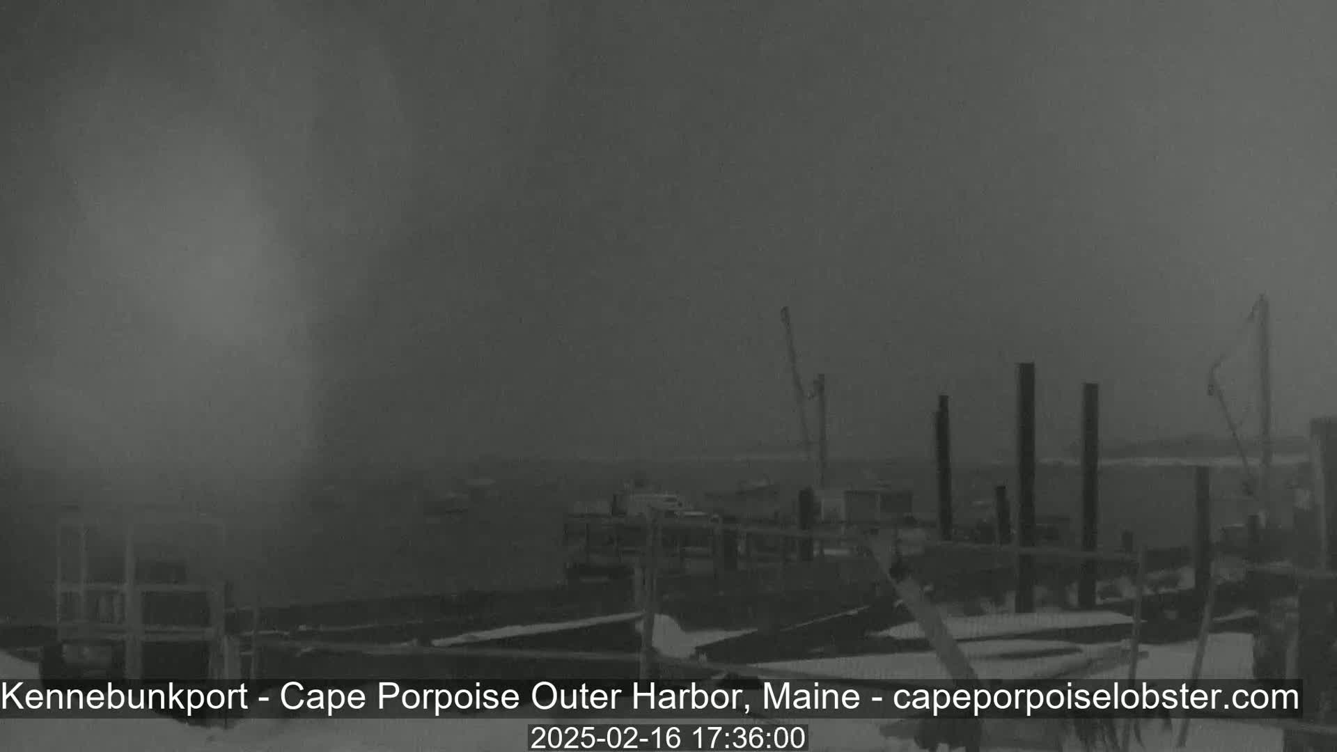 A snow-covered harbor with a pier and boats is visible in a hazy, overcast atmosphere.