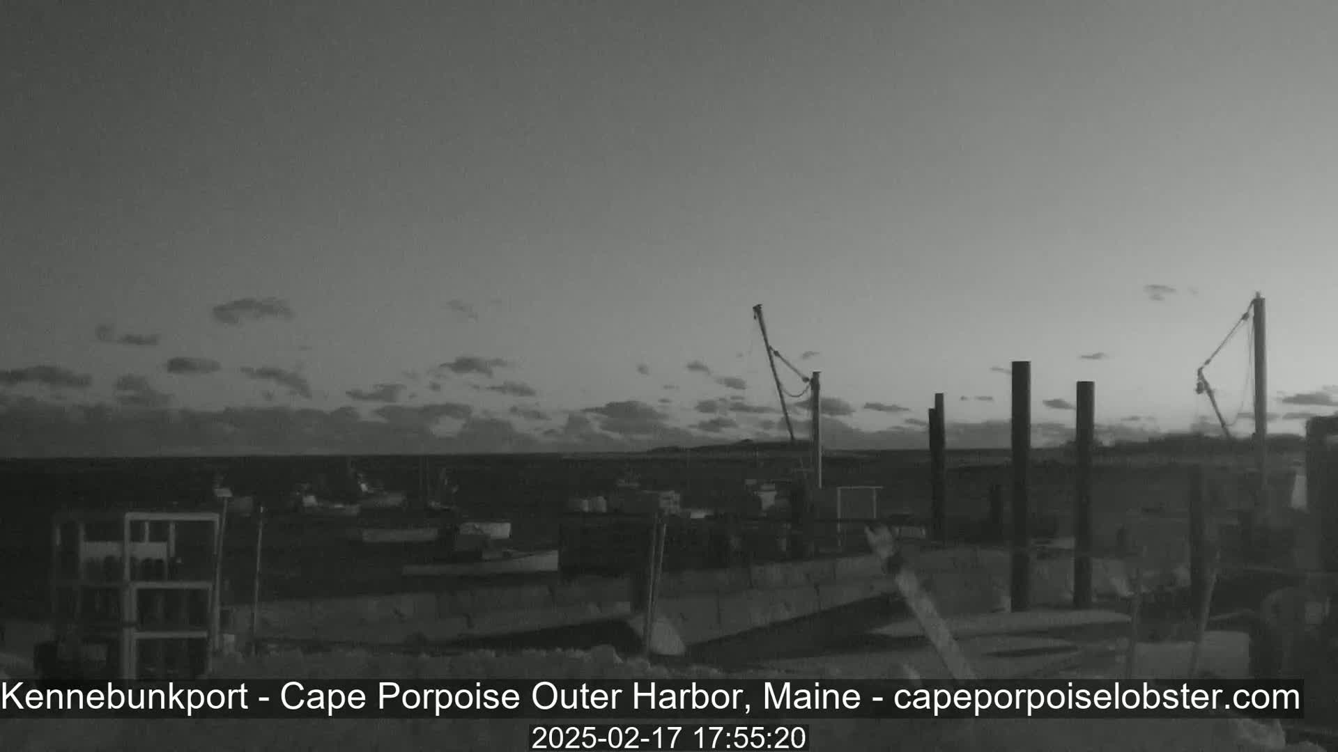 A mostly cloudy twilight sky overlooks a harbor with several boats and dockside structures.