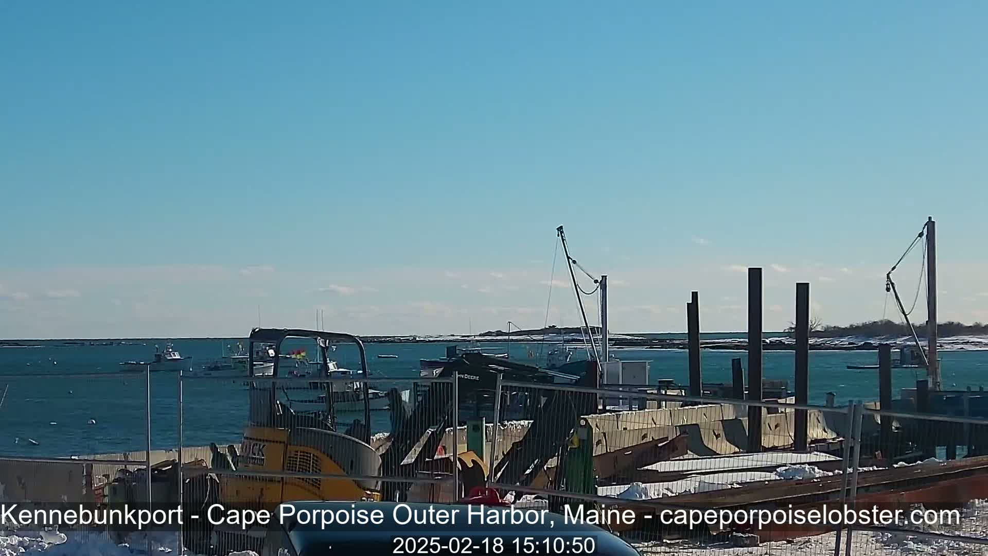 A harbor with several boats, construction equipment, and a partially constructed dock is visible under a clear blue sky.