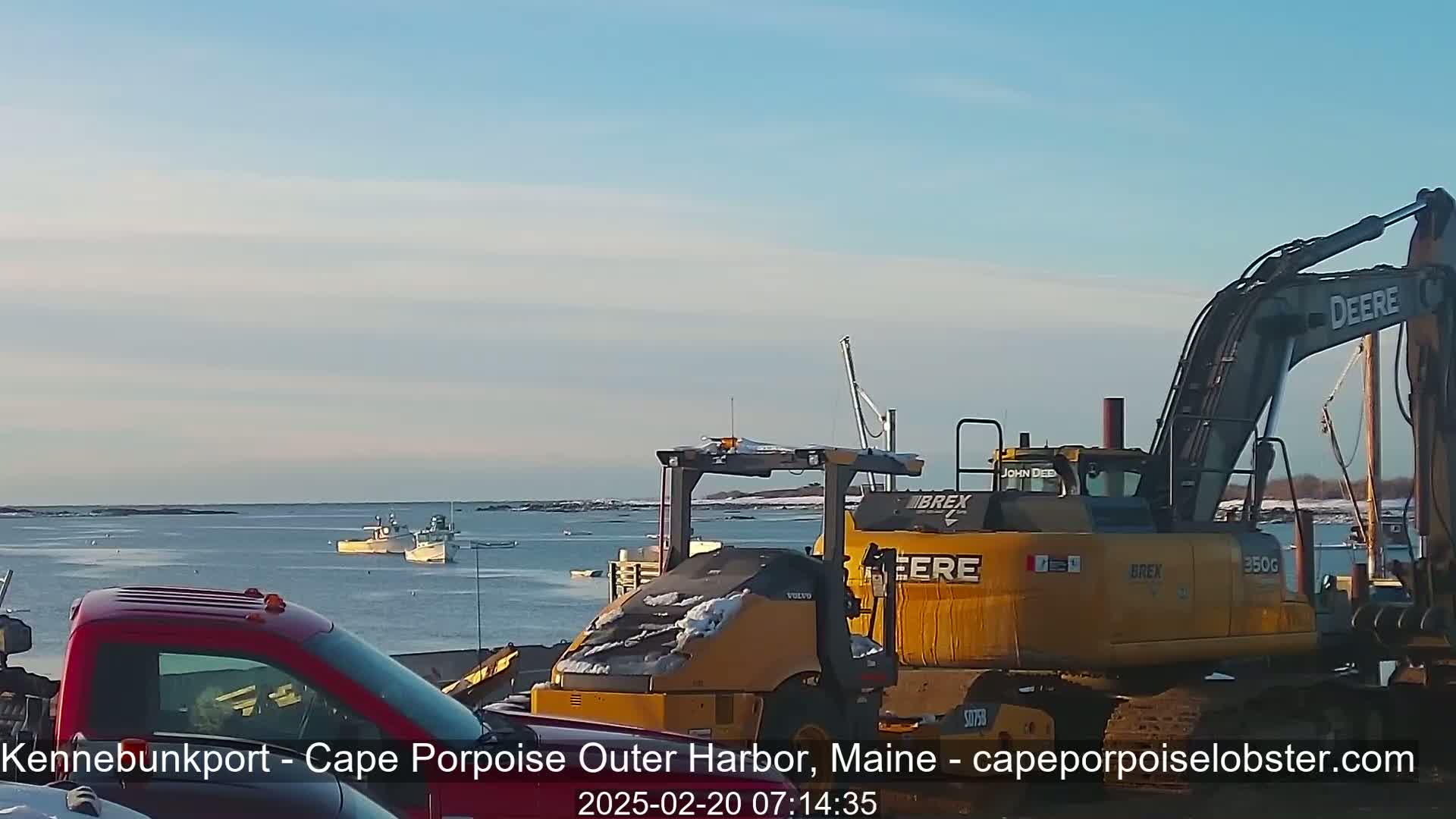 A harbor scene with two boats in calm water under a clear sky, featuring construction equipment including an excavator and a yellow loader, and a red pickup truck.