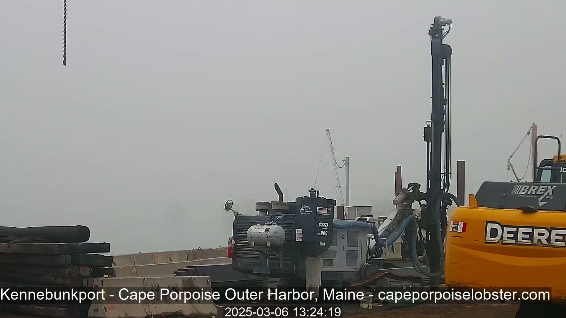 Heavy machinery, including a large drill and excavator, sits in a foggy harbor.