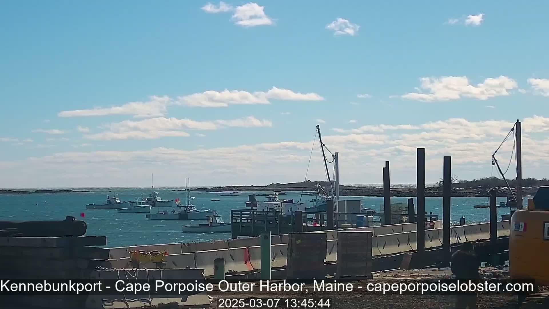 Several fishing boats are moored in a harbor under a mostly sunny sky with a few scattered clouds.