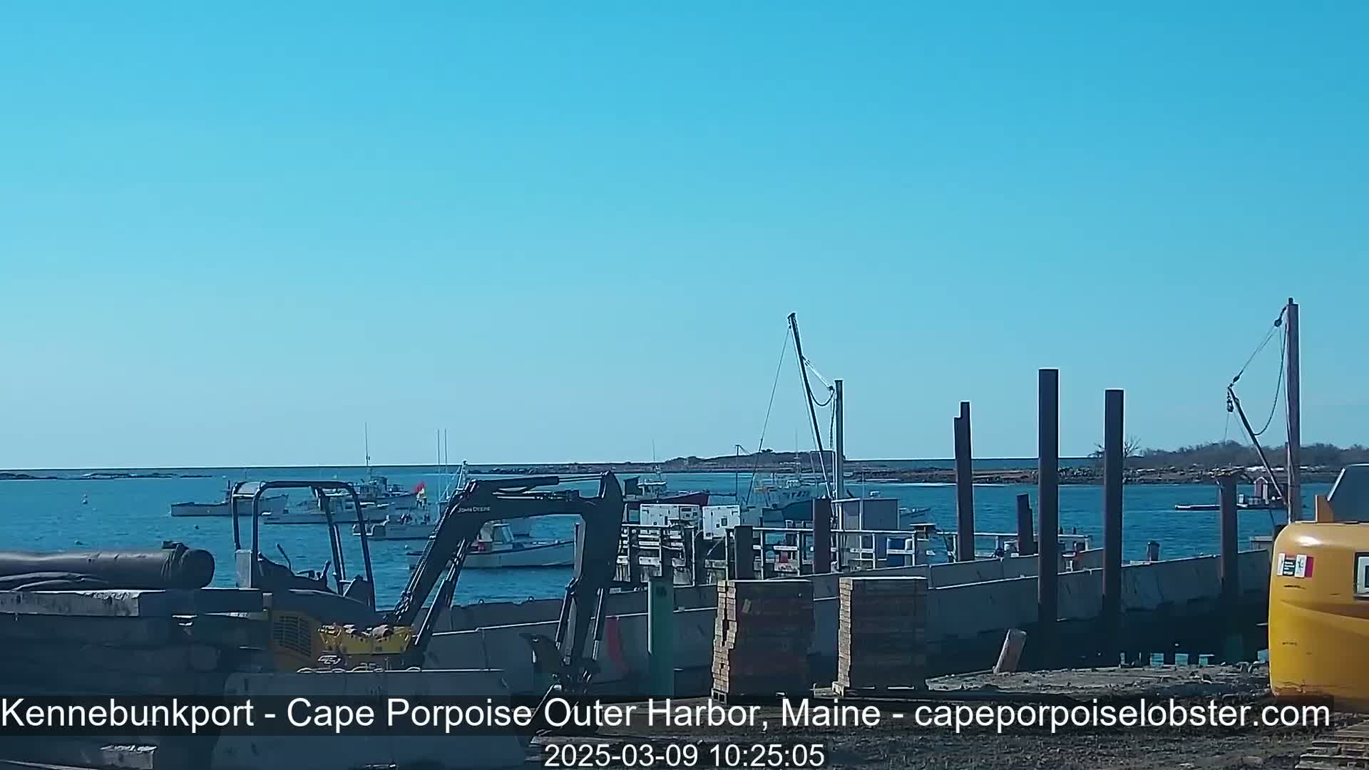 A sunny day at a harbor shows construction underway on a dock with several boats moored nearby.