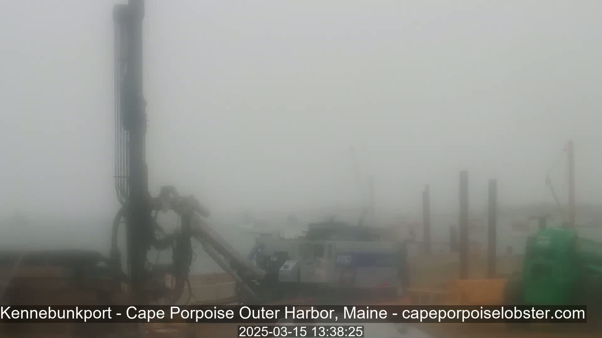 Heavy fog obscures the view of several pieces of heavy machinery and pilings at a harbor.