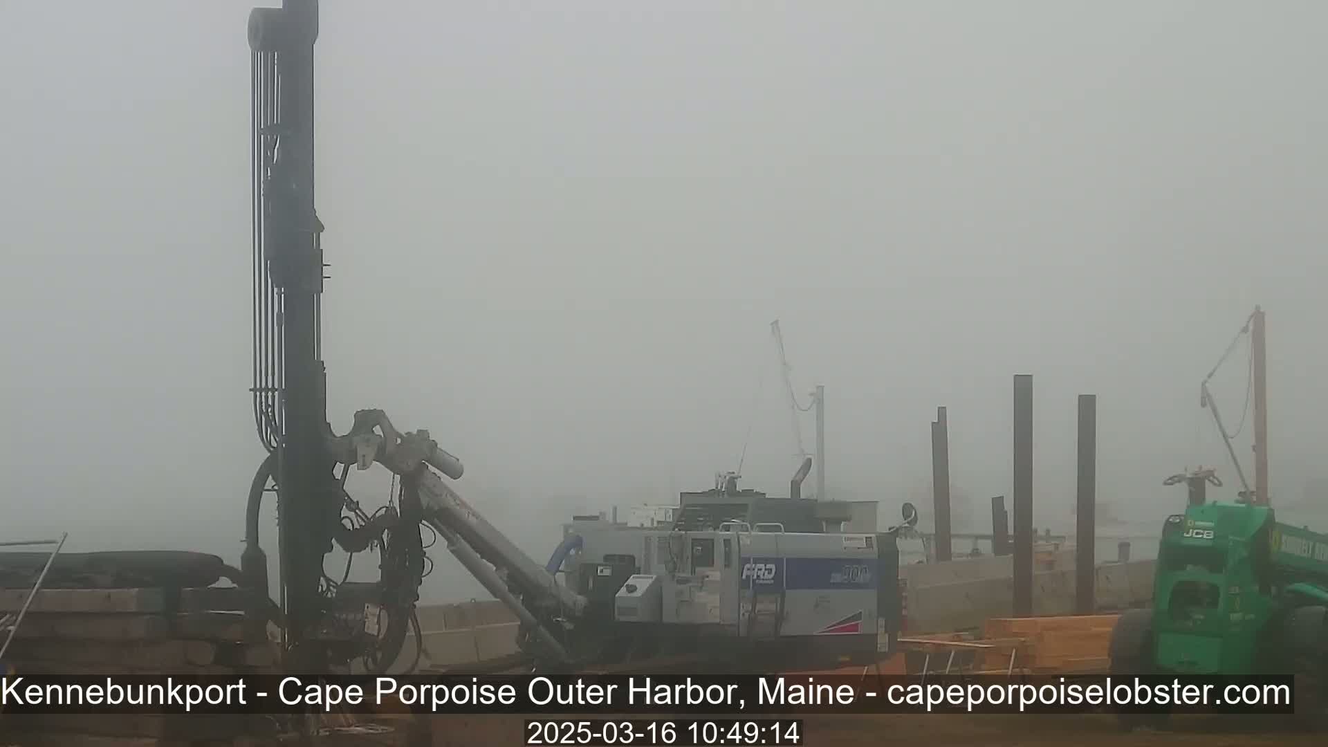 Heavy machinery, including a large drill and a crane, is visible in a foggy outdoor setting.